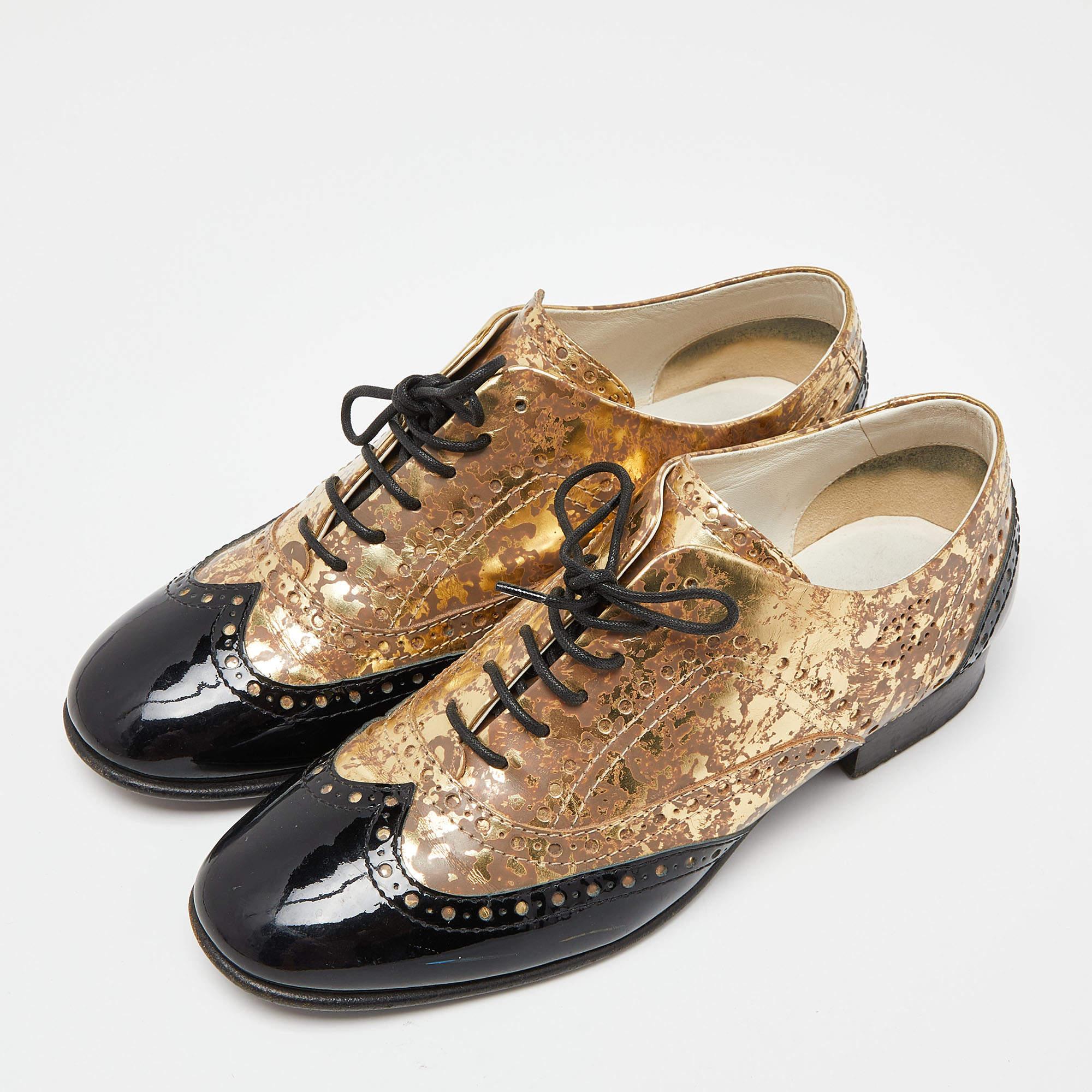Brimming with excellence and expertise, these oxfords from the House of Chanel truly embody the fine art of shoemaking. They are designed using metallic gold-black patent leather. They come with lace-ups and Brogue detailing. These oxfords are a