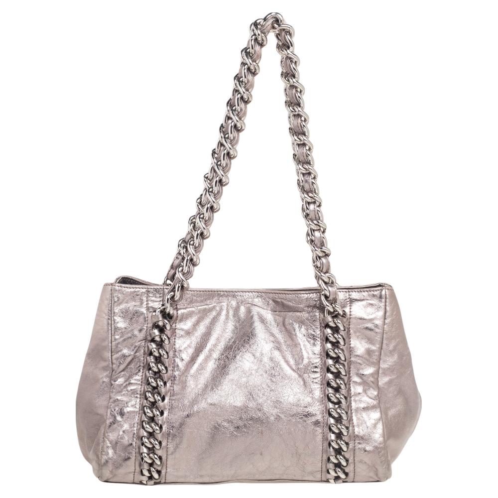 This elegant Modern Chain East/West satchel from Chanel will make a standout addition to your collection. The bag features dual top handles, protective metal feet, a CC lock, and a metallic grey leather exterior. It has a spacious fabric-lined
