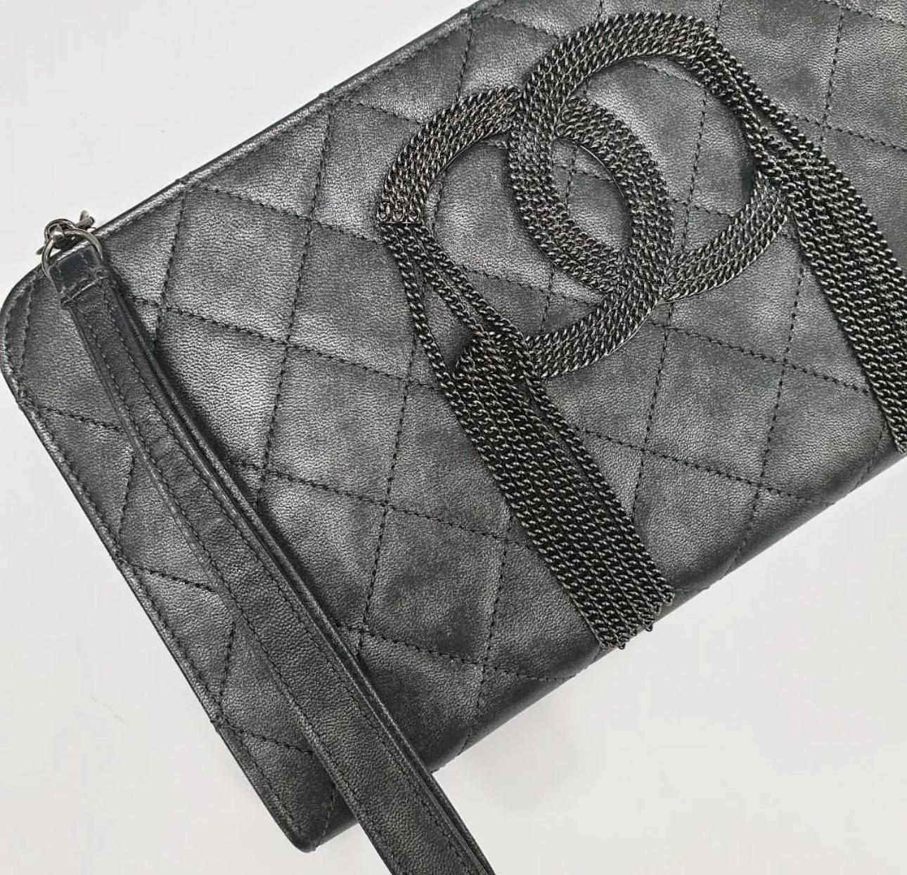 This is an authentic Chanel  Metallic Quilted Calfskin Chain CC Wristlet Clutch Black.This clutch is quilted from  leather that is accented with a stylish antiqued chain Chanel logo. Making this clutch handy is a wrist-let stitched on to the top