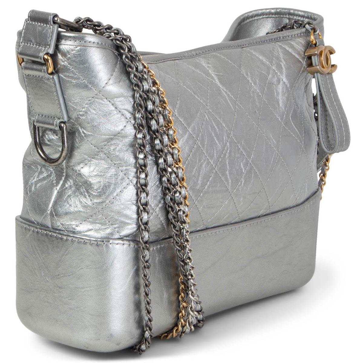 100% authentic Chanel Gabrielle Medium Hobo Bag in metallic silver aged calfskin featuring doubel chain shoulder-strap in gold-tone, silver-tone & ruthenium-finish metal. Opens with a CC zipper on top and is lined in red grosgrain fabric with one