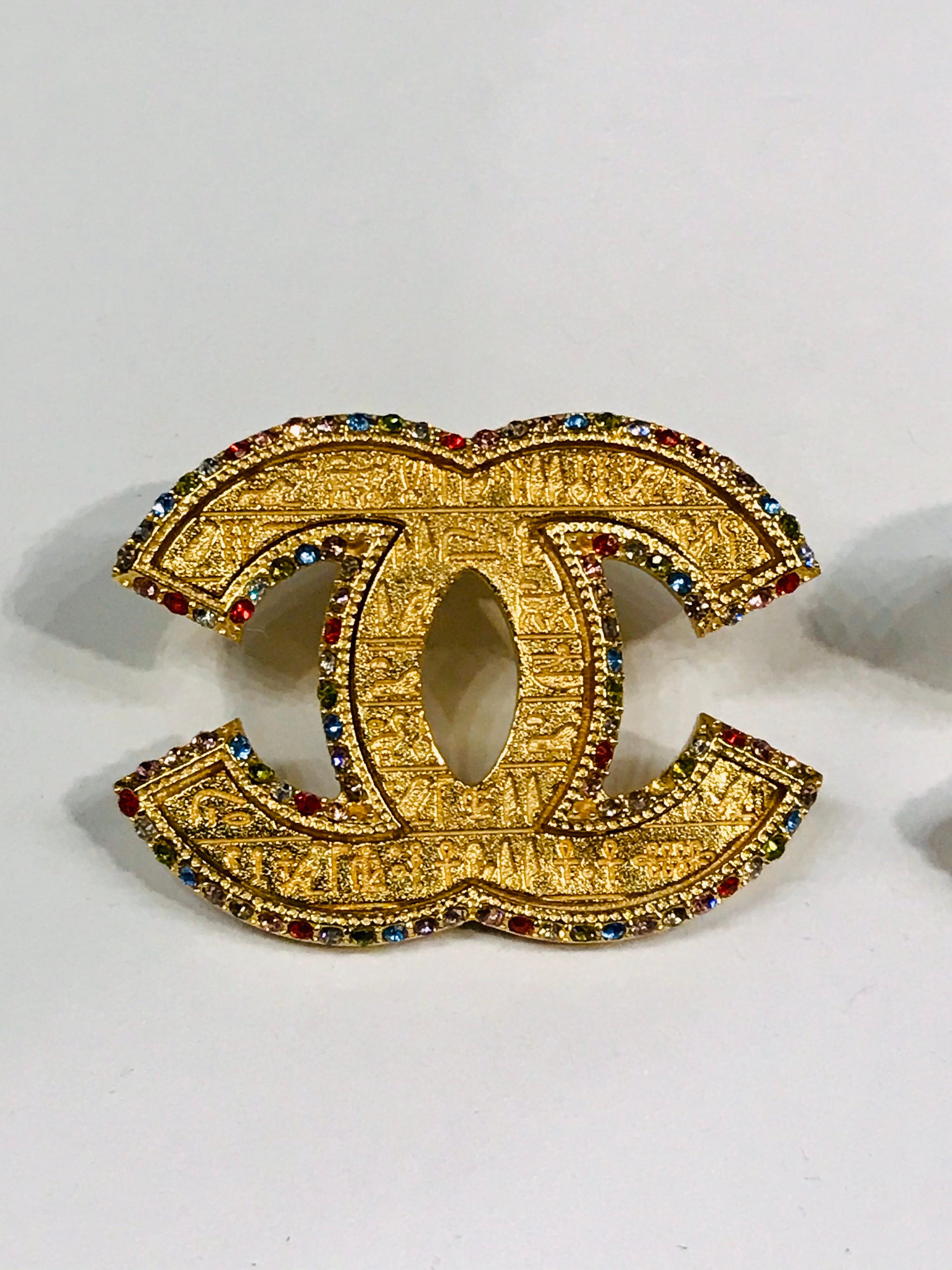 From the 2019 Metiers d’Art collection is this lovely pair of Chanel interlocking CC logo earrings inscribed with Egyptian hieroglyphs and  ser with multicolor rhinestones in red, green, blue, pink, clear and smoke. Each earring measures 1.24 inches
