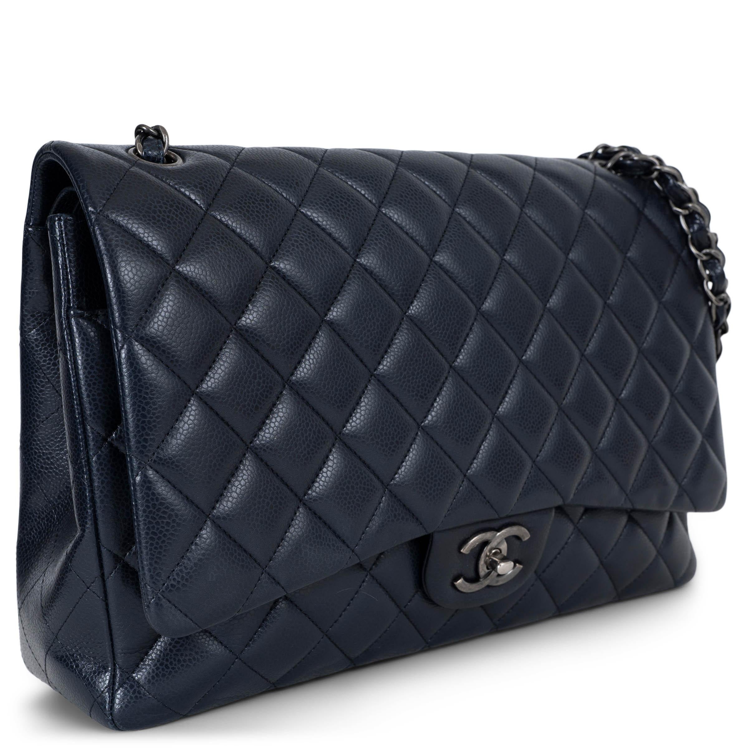 Ce sac Chanel Classic Maxi à double rabat, 100% authentique, est réalisé en cuir Caviar matelassé de diamants bleu nuit avec des accessoires en ruthénium. Il présente les détails emblématiques de la maison : une poche ouverte au dos, une bandoulière