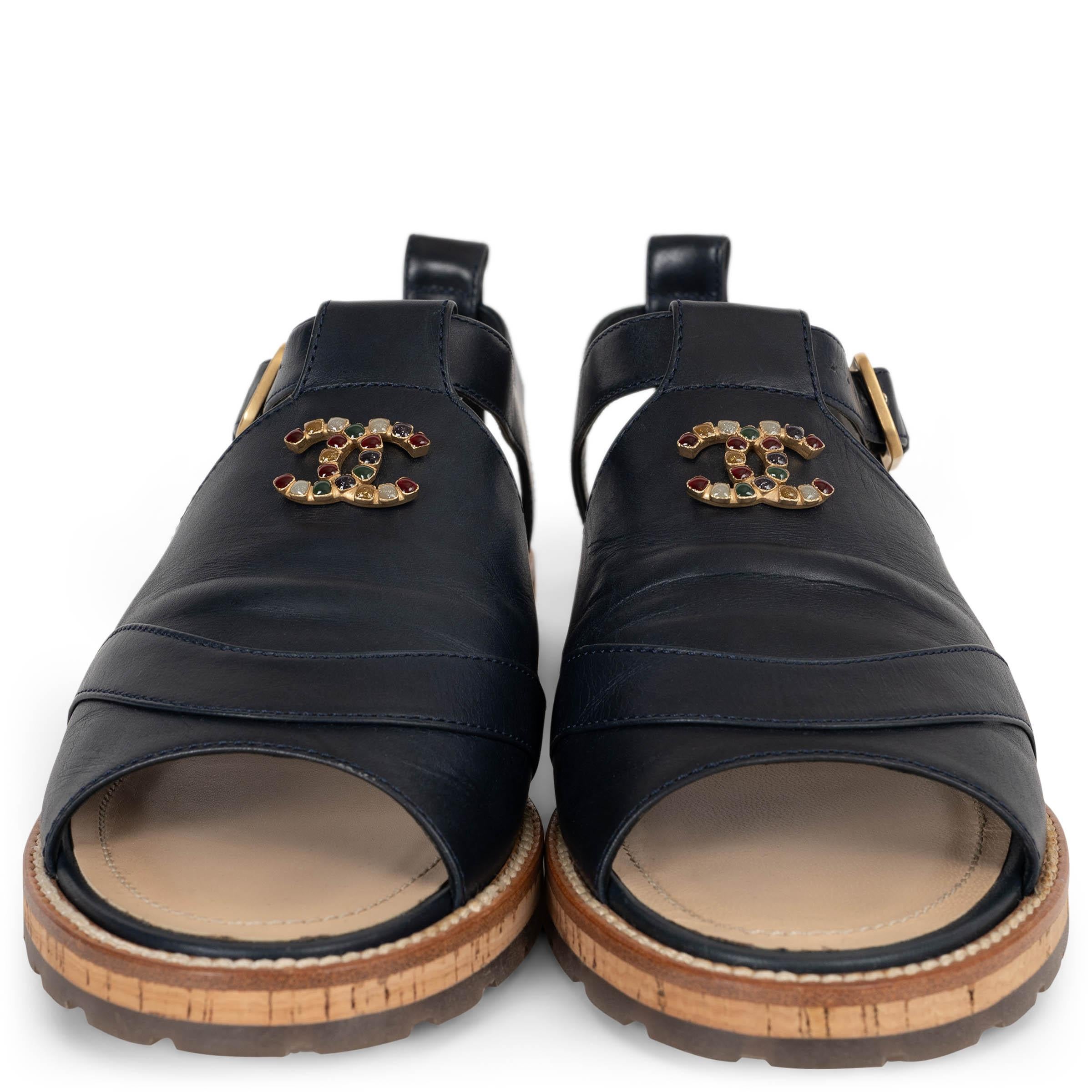 Diese 100% authentischen Chanel-Sandalen aus nachtblauem Glattleder sind mit einem auffälligen CC-Monogramm versehen, das mit mehrfarbigen Steinen appliziert ist und einen verspielten und zugleich eleganten Touch hat. Das Design steht auf einer