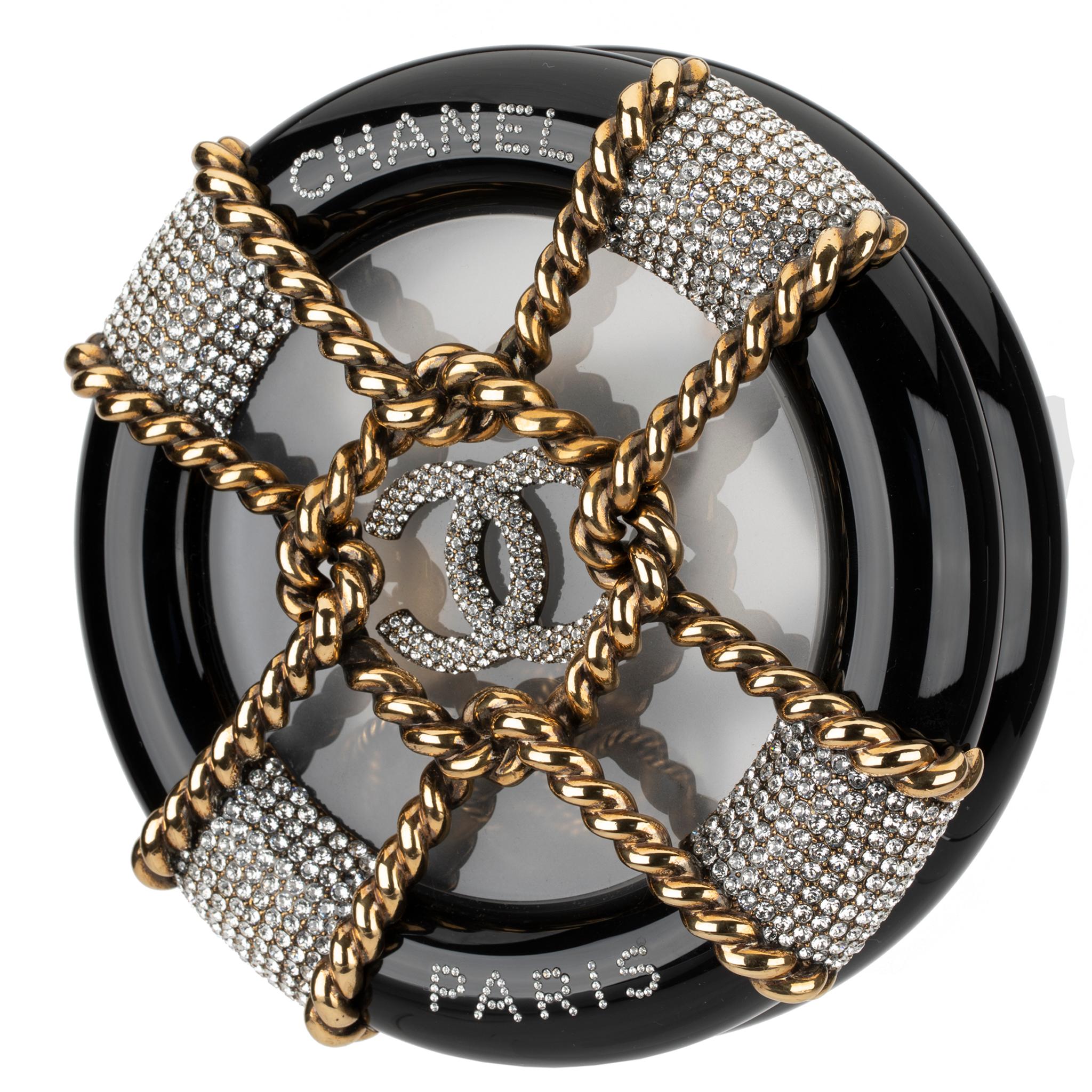 The Chanel Rescue Wheel Minaudiere is skilfully crafted from lucite. Inspired by nautical origins, the design features rhinestones, the iconic double C logo, intertwined gold rope and a frosted window centre. A push button clasp opens to reveal
