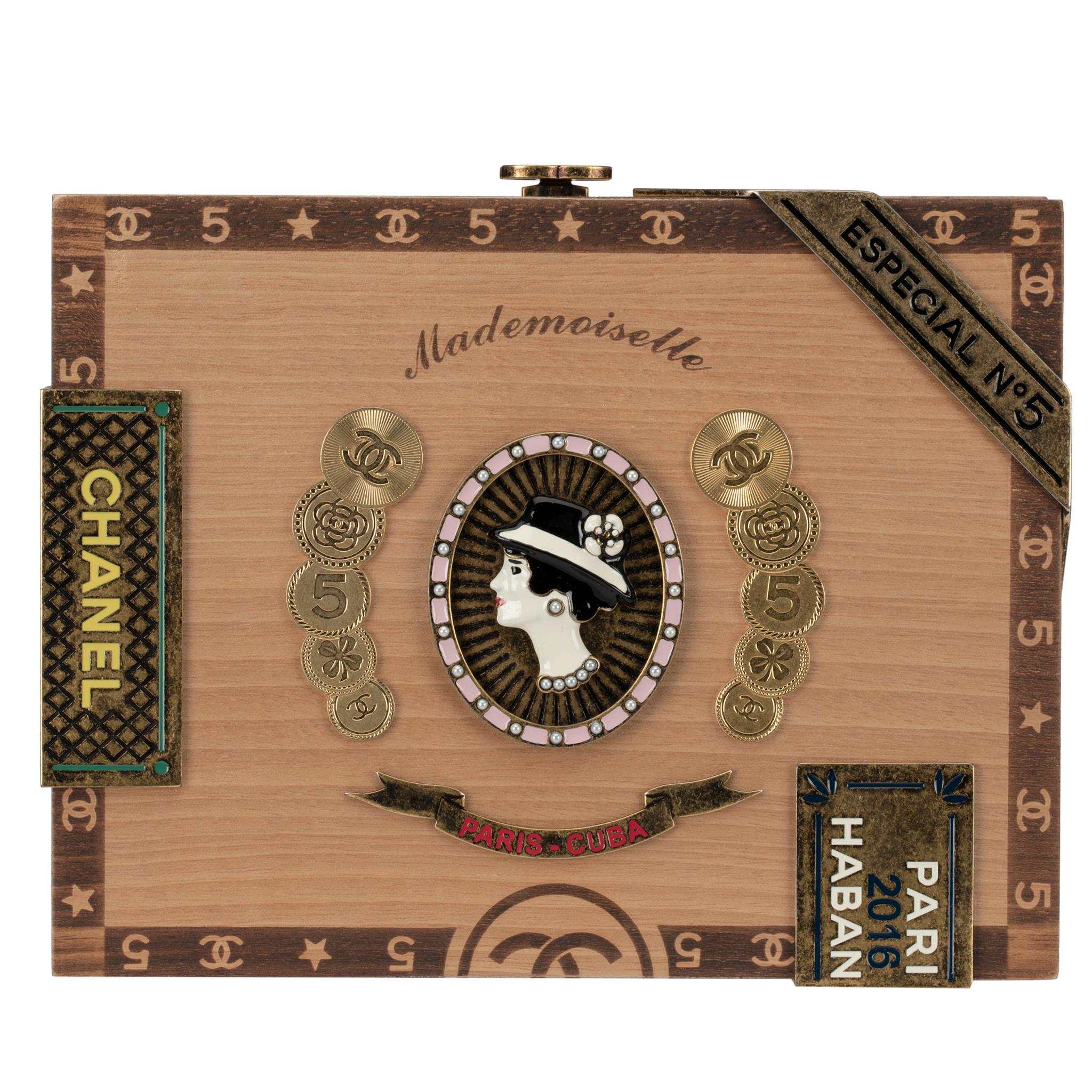 Skilfully crafted from natural walnut wood, this collectable minaudière is designed to resemble a Cuban Cigar Box. Adorned with antique gold-tone hardware and multi-coloured medallions – at the front centre a portrait of Mademoiselle Coco Chanel