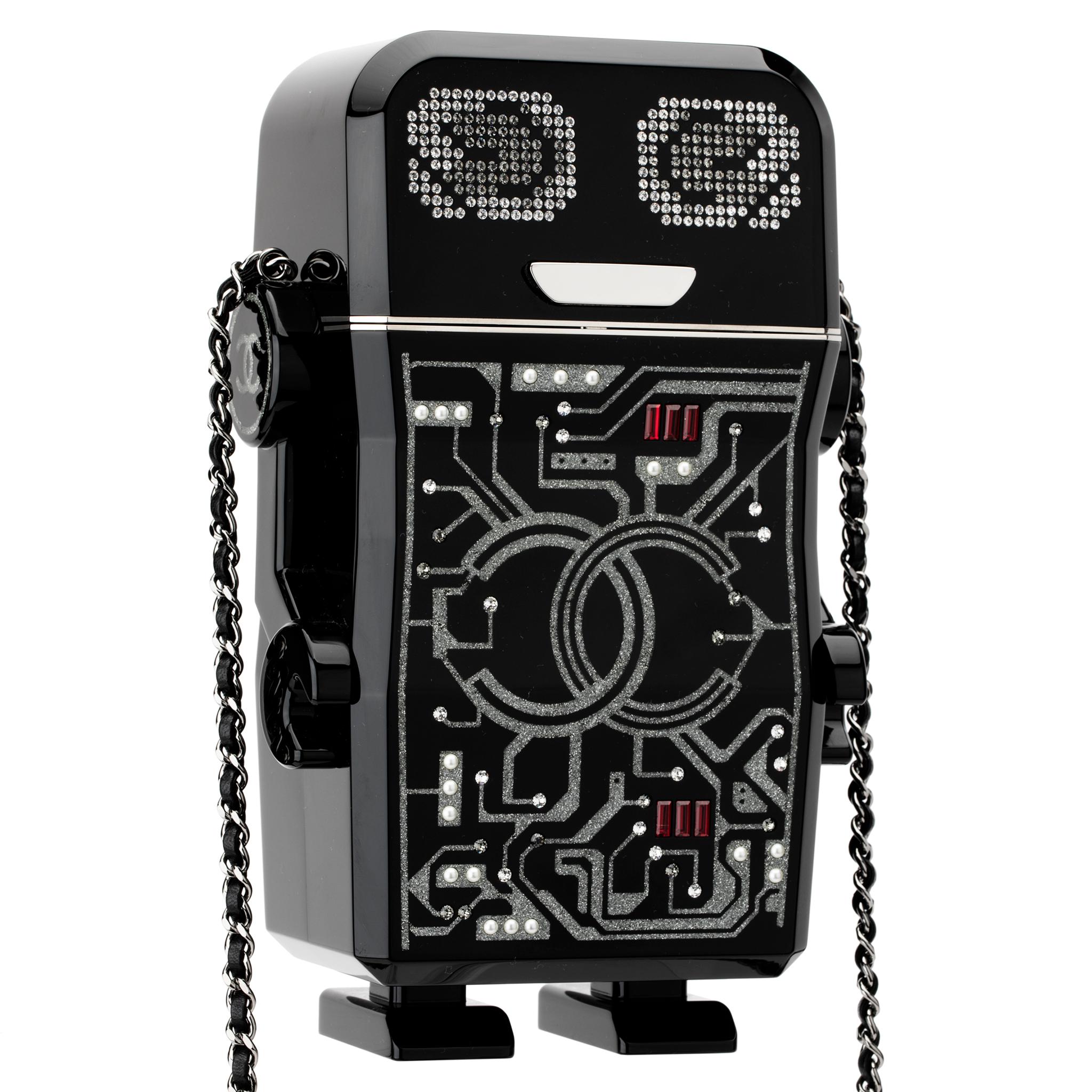 Ti presentiamo il nuovo robottino di Chanel, non ha ancora un nome ma sta a te deciderlo. Questo personaggio futuristico è impreziosito da dettagli glitterati, strass rossi e dal logo a doppia C di Chanel. La bocca funge da chiusura a pressione, che