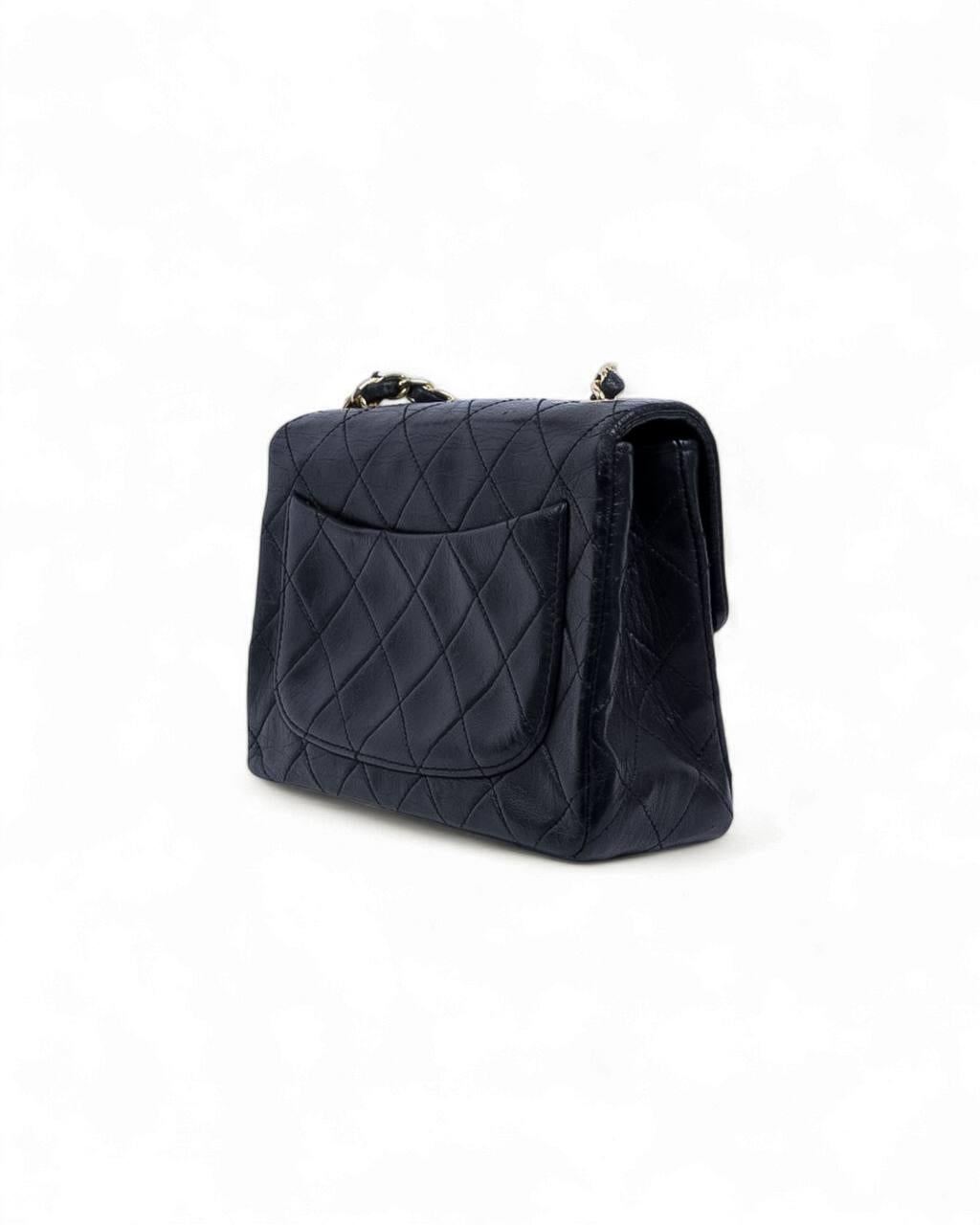 Bolso Chanel modelo Timeless Mini Flap Vintage, realizado en piel negra lisa con herrajes dorados. El bolso presenta una solapa con cierre giratorio con el logotipo CC, mientras que el interior está forrado en suave piel burdeos, con espacio