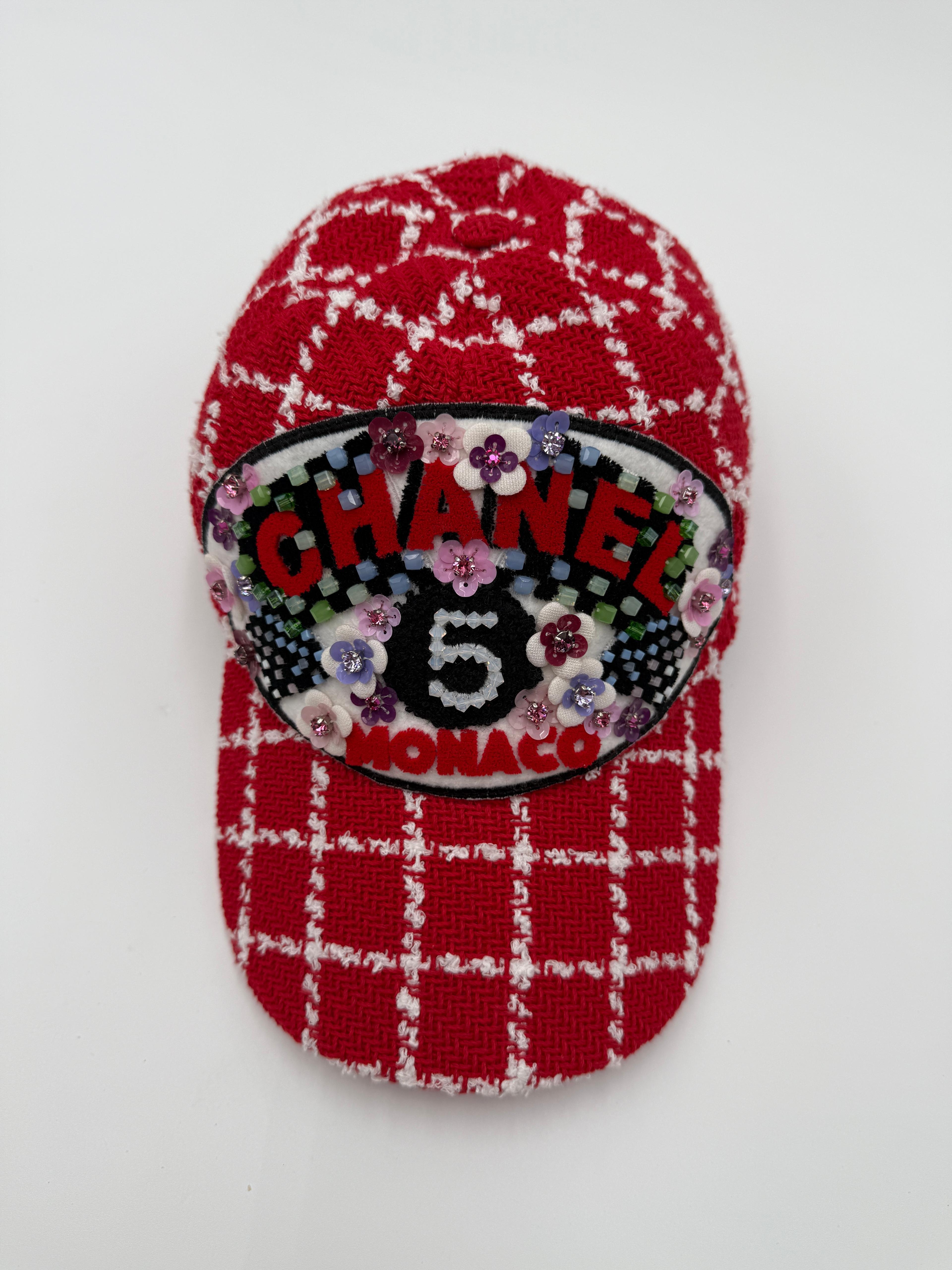 This ultra-rare Chanel cap features a vibrant red and ivory woven tweed base with a bold checkered pattern. The standout detail is the oversized embroidered patch reading CHANEL 5 MONACO, intricately adorned with multicolor sequins and layered