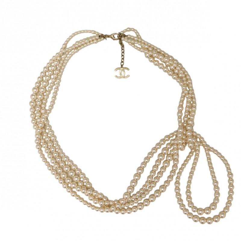 Ce collier Chanel est un long collier de perles à plusieurs rangs, de couleur nacrée. Les bijoux sont en métal plaqué or clair. La forme est asymétrique avec quatre rangs de perles, CC bijou sur le fermoir. Un nœud de perles fait un pendentif sur le