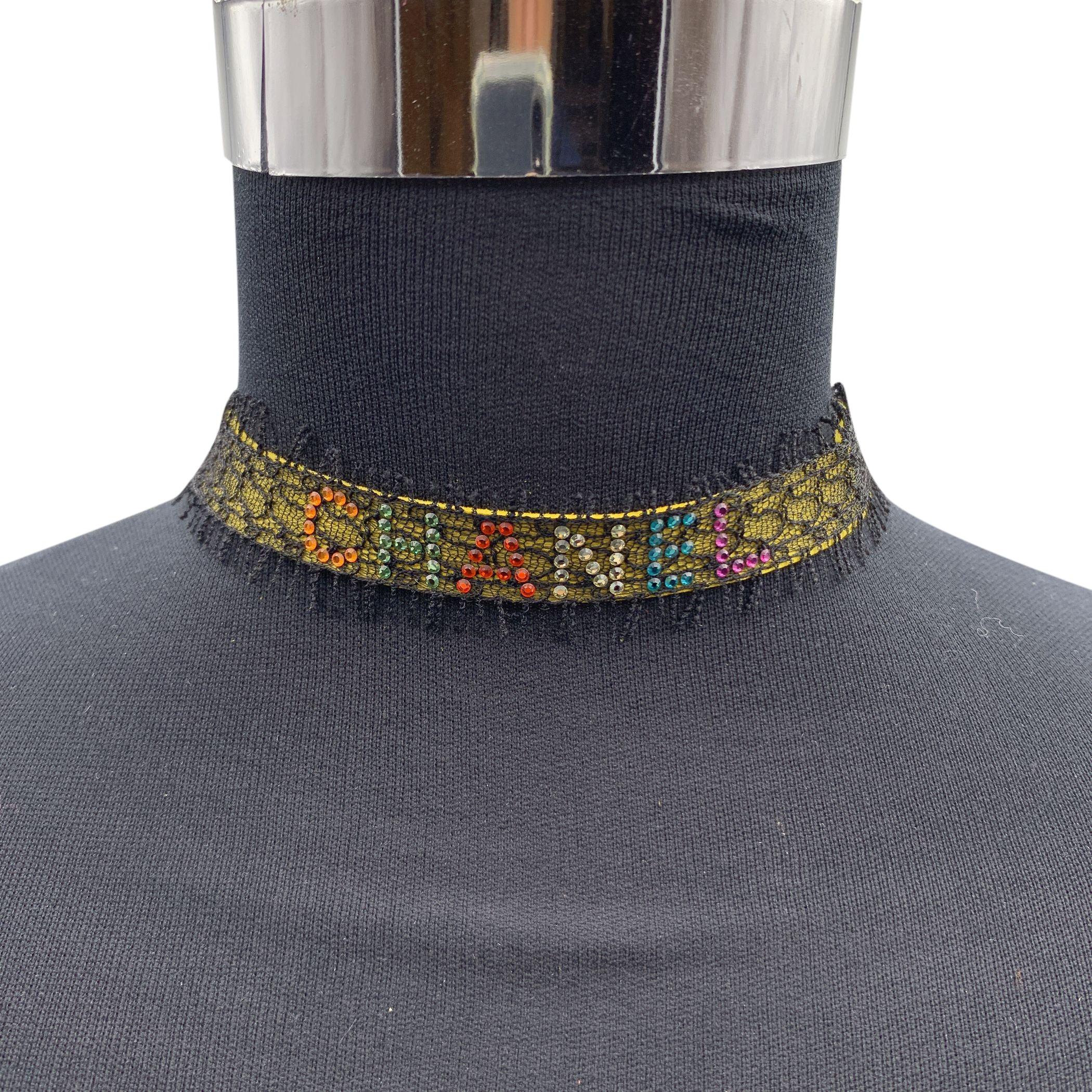 Chanel ribbon lace choker necklace lined in yellow suede. It features a multicolor rhinestone Chanel writing on the front. Silver chain link closure with CC logo. Hook closure. Adjustable. Max length: 13.5 inches - 34.3 cm. 'CHANEL - 00 CC T - Made