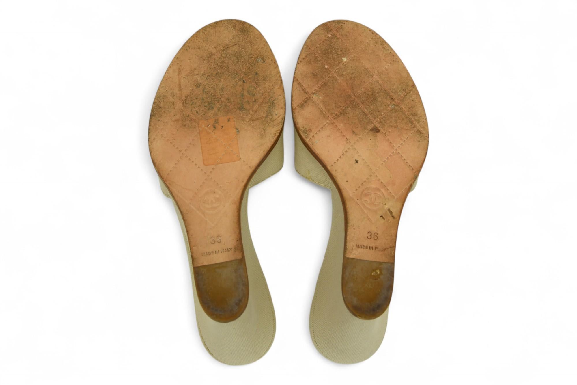 Sandalias de cuña Chanel Natural Canvas CC Logo Slide en un versátil tono beige, con el icónico logotipo CC entrelazado bordado en la tira delantera. Fabricadas en lona resistente, con plantillas forradas de piel para mayor comodidad y un tacón de