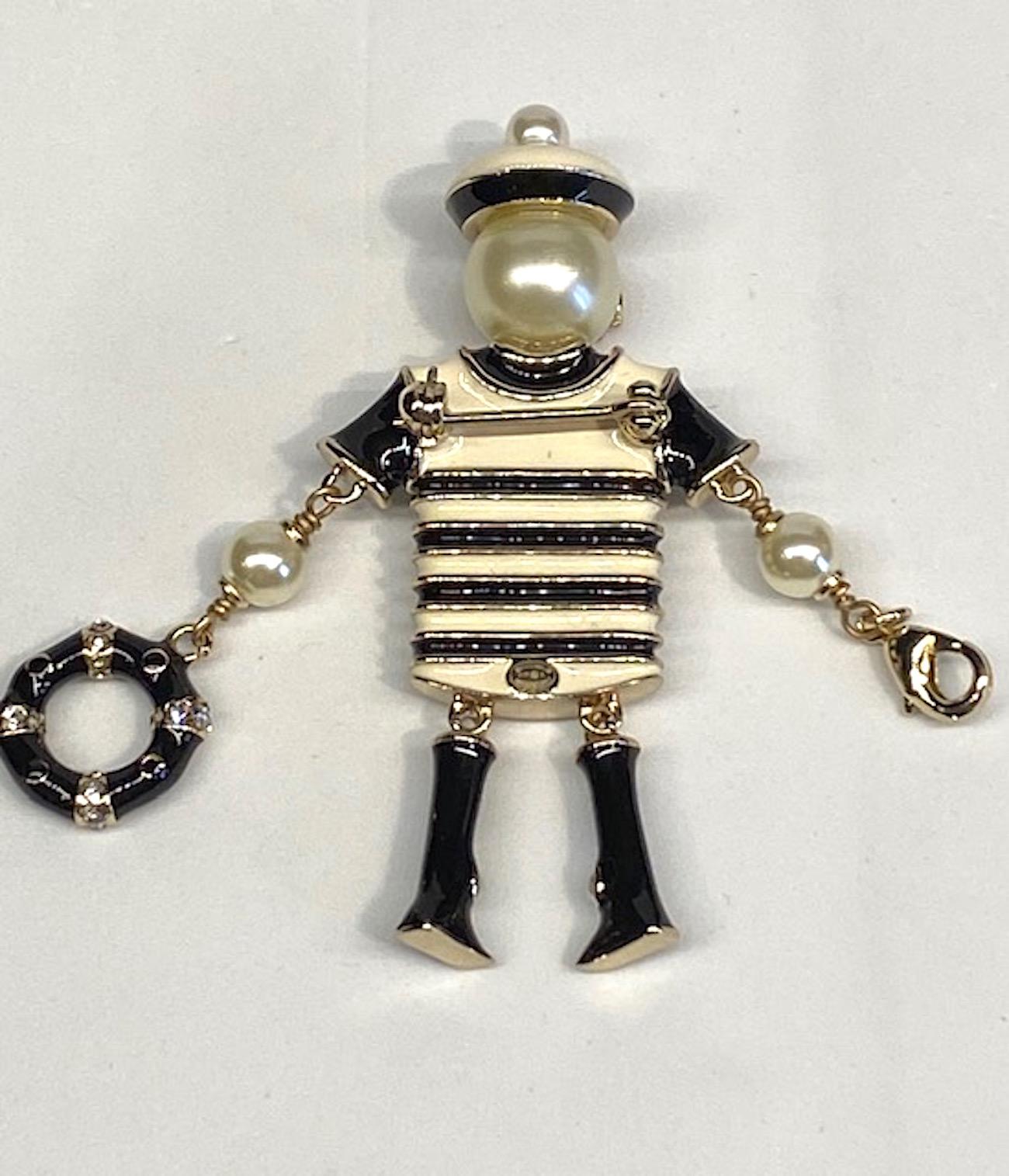 A charming Chanel figural pin with nautical interpretation of Madame Coco Chanel in a beret. The gold plate brooch is enameled in ivory, black and pink. The Chanel iconic interlocking CC logo is set with rhinestones. The head is a large faux pearl