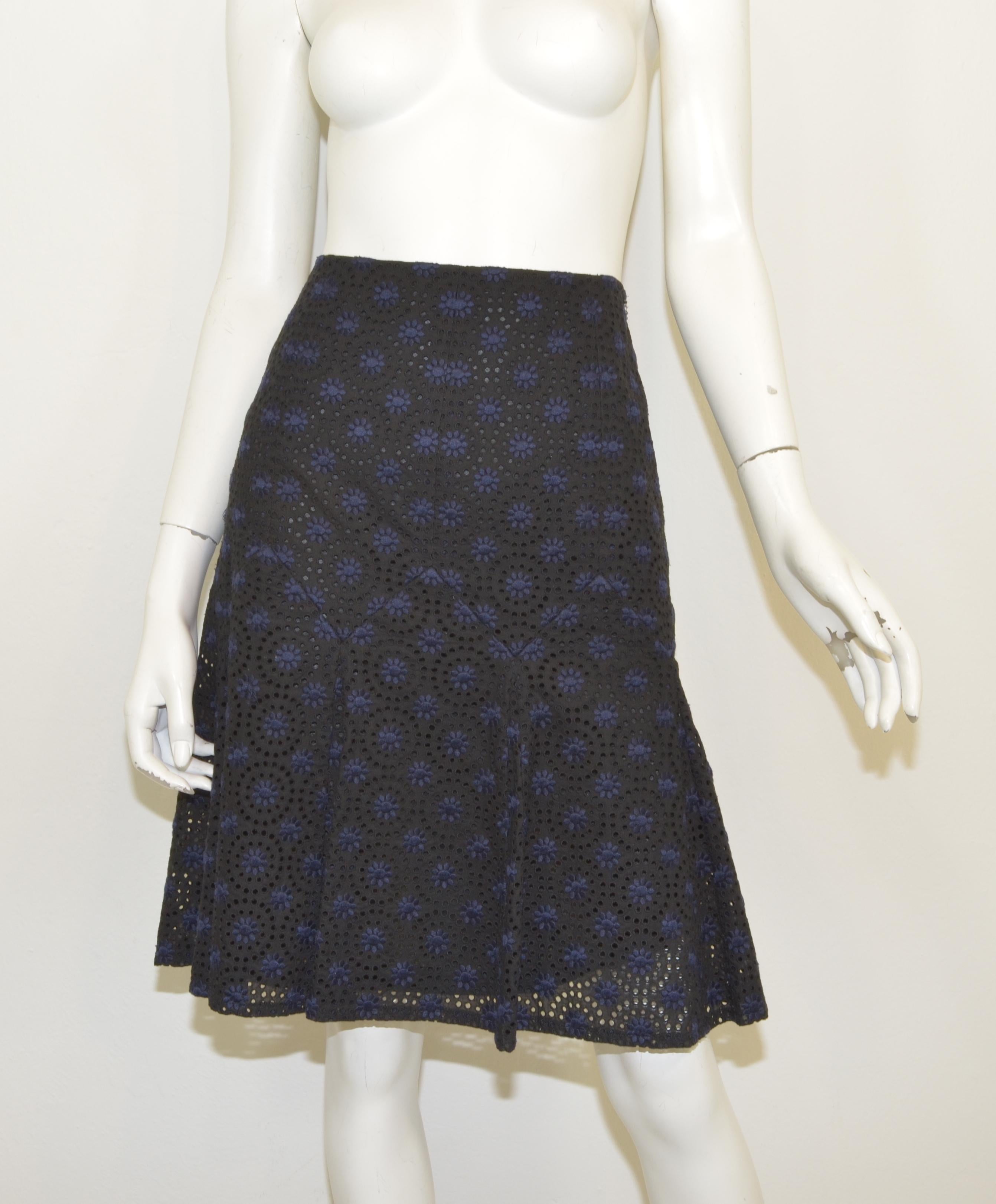 Chanel eyelet skirt is featured in navy and black with a floral design, pin tucked hem, back zipper and hook and eye fastening, and a full cotton lining. Skirt is a size 40, made in France, composed with a cotton and polyester blend.