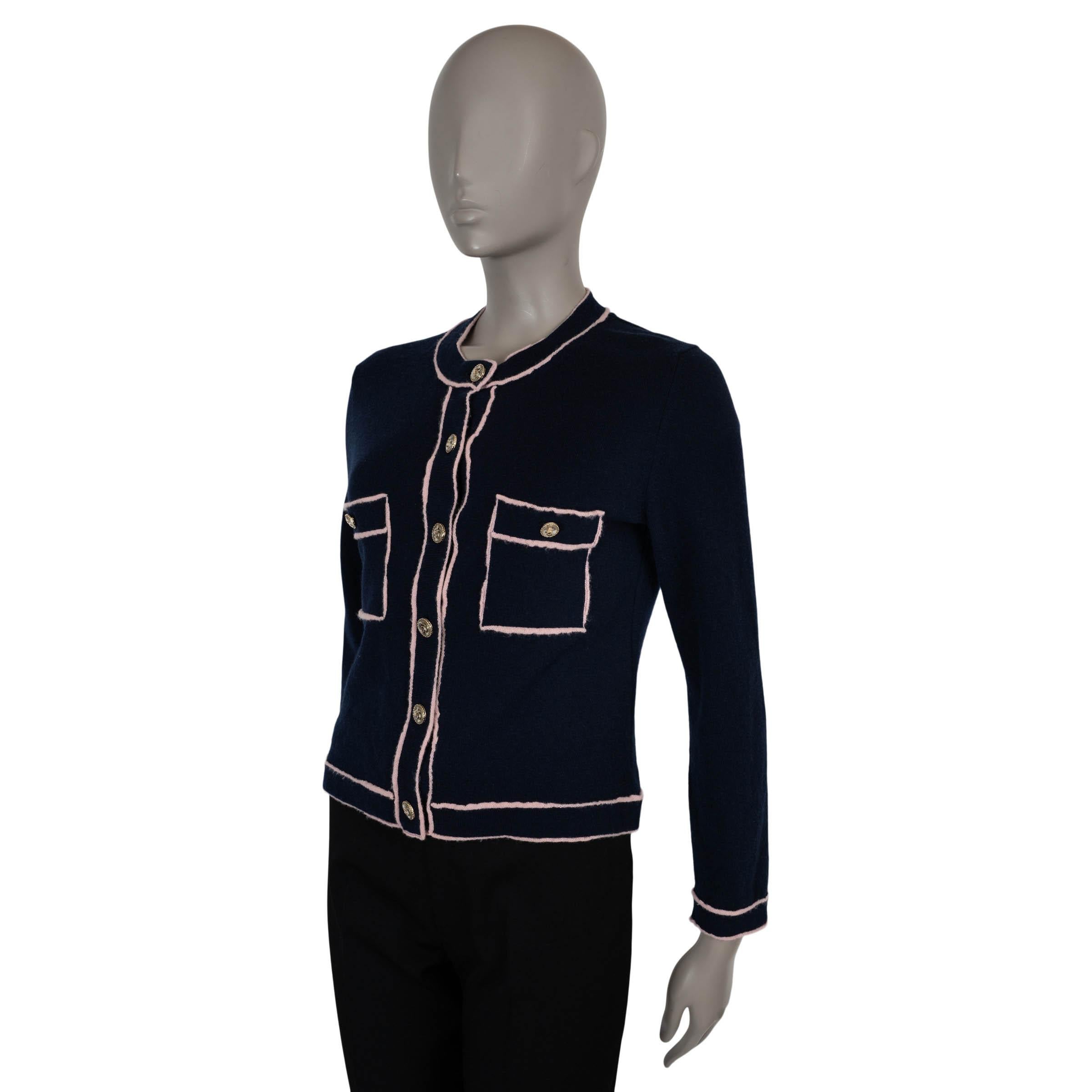 This 100% authentic Chanel cardigan in navy blue cashmere (100%) is accented with contrasting light pink outlined seams for a refined finish. Designed with a classic fit and crew neckline, it features two buttoned chest pockets and closes with