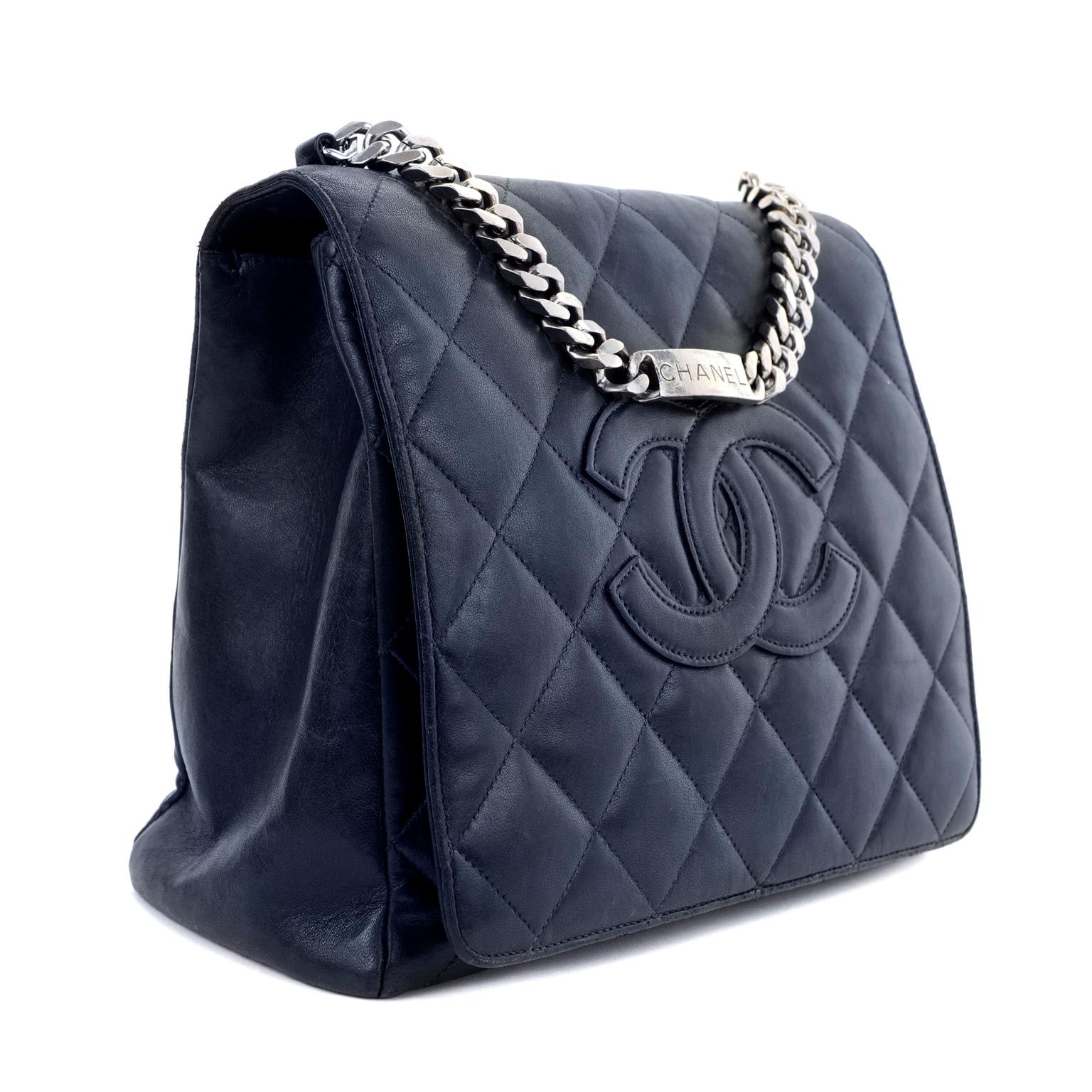 This authentic Chanel Navy Blue Lambskin Top Handle Flap Bag is in very good condition.  Regal navy-blue lambskin is quilted in signature Chanel diamond pattern with large interlocking CC tonally stitched in the center.  Substantial silver tone curb