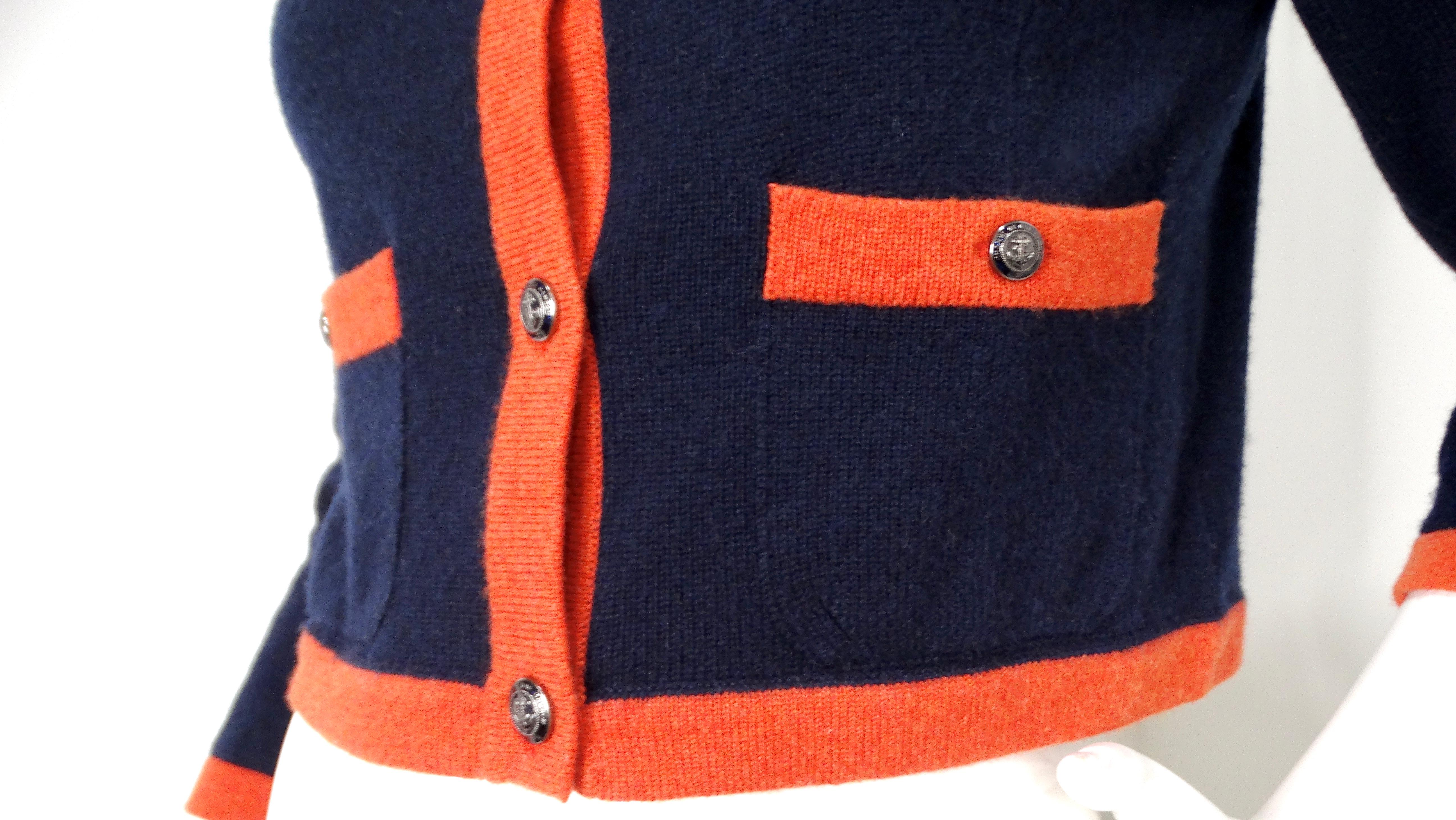 Die marineblau-orangefarbene Kaschmir-Strickjacke von Chanel ist ein luxuriöses und raffiniertes Stück, das die zeitlose Eleganz und die Liebe zum Detail von Chanel verkörpert. Diese Strickjacke ist aus weichem Kaschmir gefertigt und bietet Komfort
