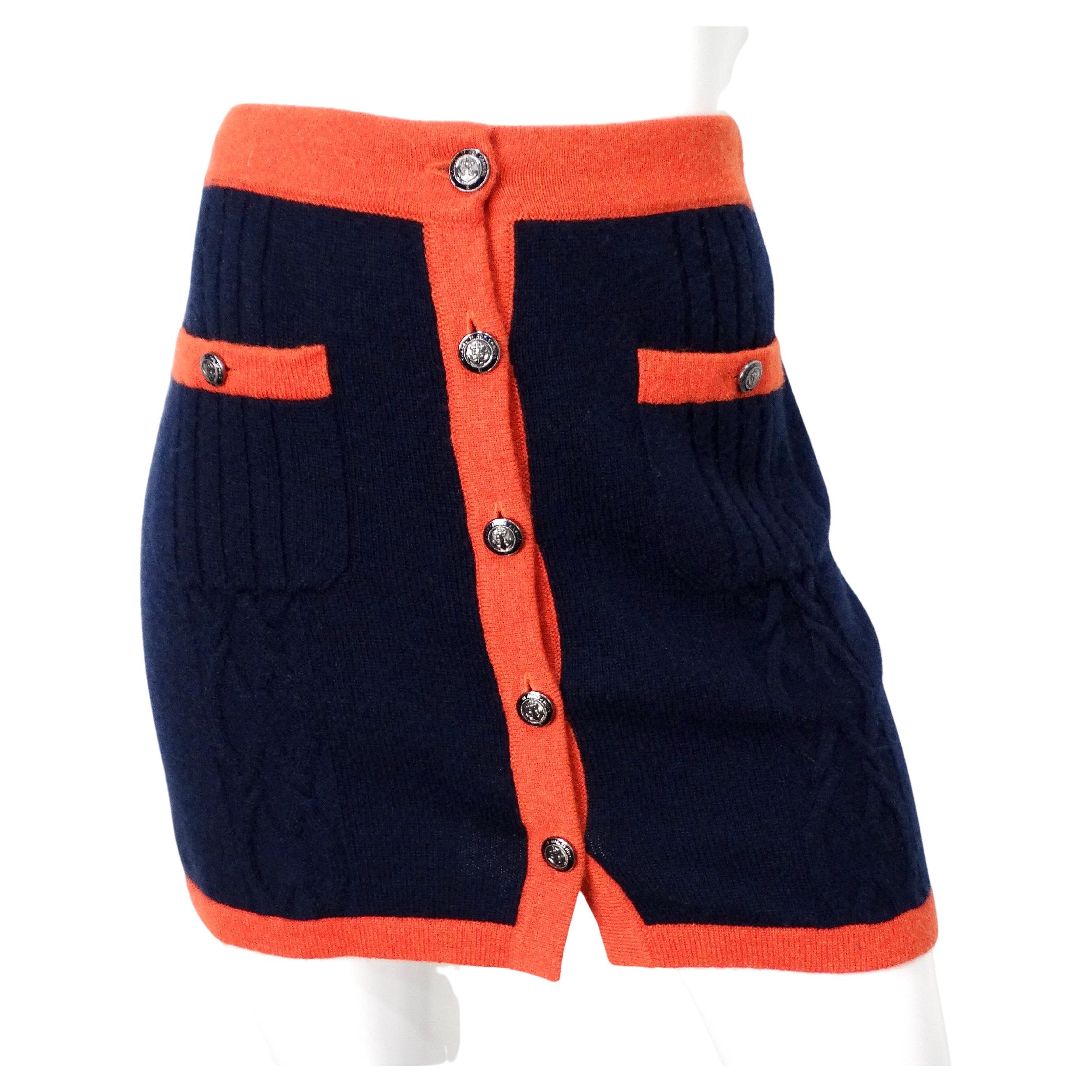 La minigonna Chanel in maglia di cashmere blu e arancione emana un'eleganza sofisticata con un tocco contemporaneo. Realizzata in lussuoso cashmere, questa minigonna presenta una ricca base blu navy accentuata da un vivace orlo arancione e da una