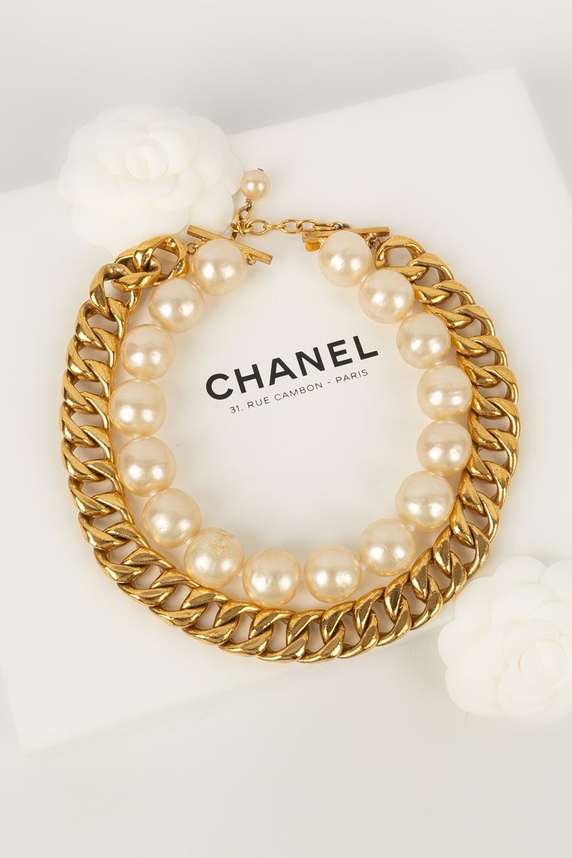 Chanel - (Made in France) Collier court composé d'une chaîne en métal doré et d'un rang de perles nacrées. Collection 2cc7 - Croisière 1991/92. A noter, les perles présentent des marques.

Informations complémentaires :
Condit : Très bon