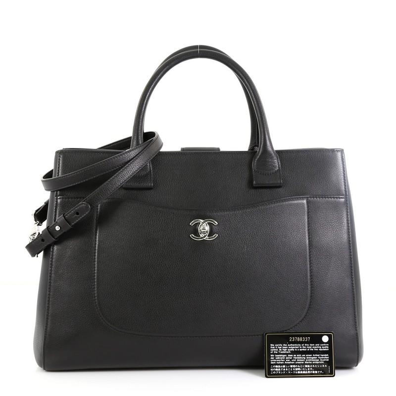 This Chanel Neo Executive Tote Grained Calfskin Medium, crafted from black calfskin leather, features dual-rolled leather handles, front pocket with CC turn-lock closure, exterior back slip pocket, and silver-tone hardware. Its magnetic snap closure