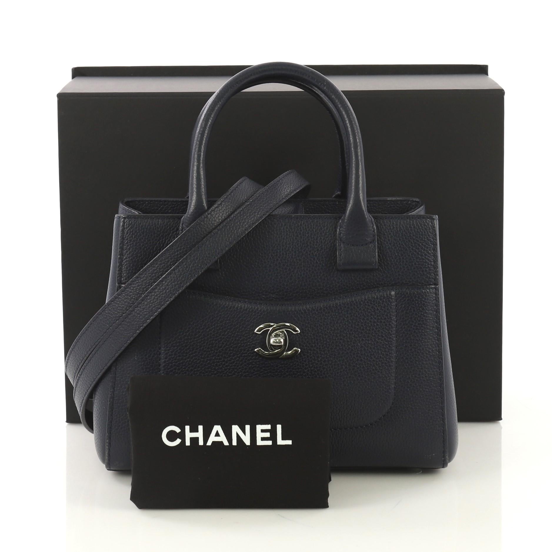 This Chanel Neo Executive Tote Grained Calfskin Mini, crafted from blue grained calfskin leather, features dual rolled leather handles, front pocket with CC turn-lock closure, and silver-tone hardware. Its magnetic snap closure opens to a blue
