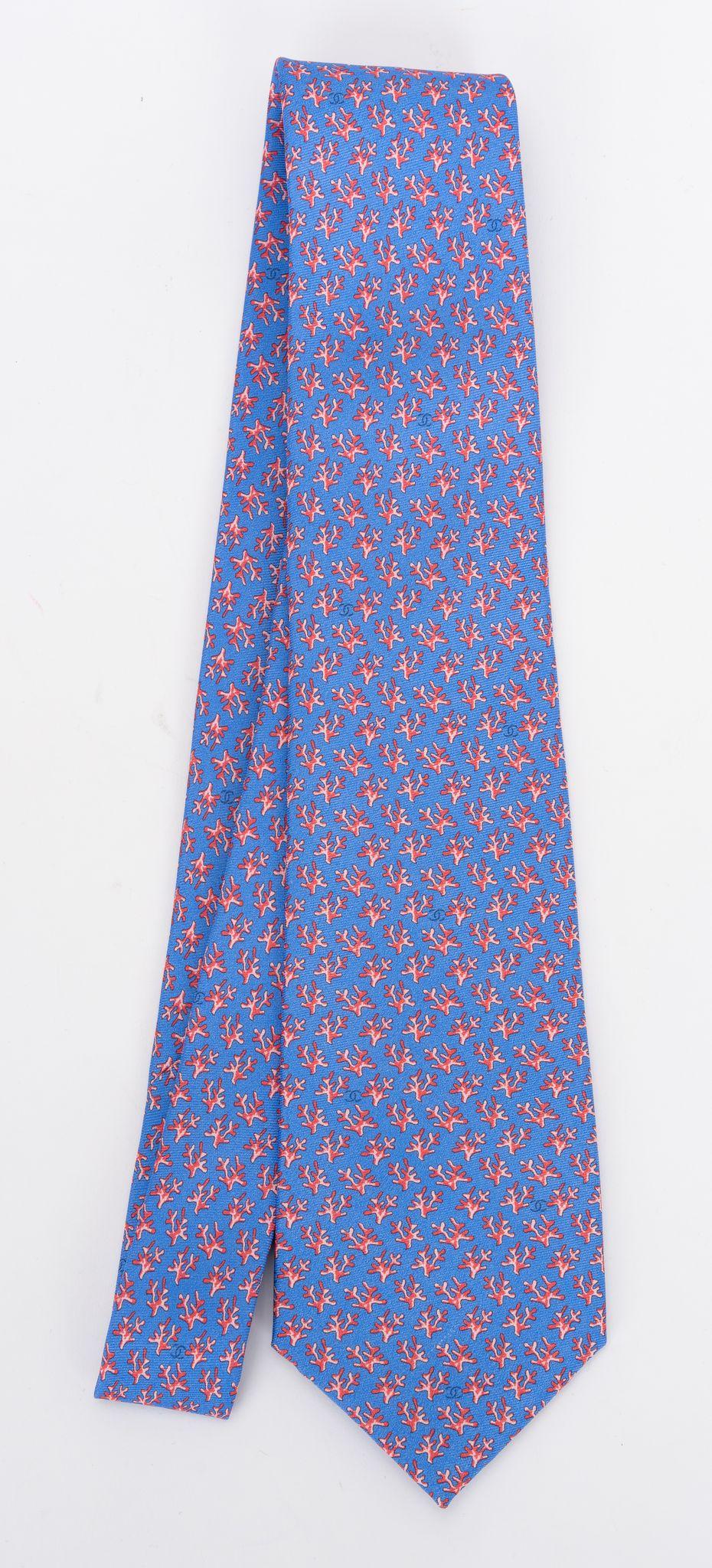 Cravate neuve 100% soie de Chanel à motif de branches de corail bleu. Label de composition, étiquette de marque et chaîne de signature. Livré avec l'enveloppe d'origine.