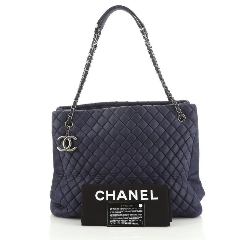 This Chanel New Bubble Tote Quilted Calfskin Large, crafted from blue quilted calfskin leather, features woven-in leather chain straps with leather pads and aged silver-tone hardware. It opens to a blue fabric interior. Hologram sticker reads: