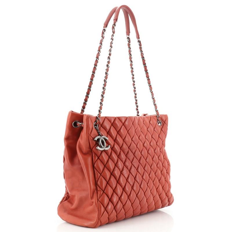 This Chanel New Bubble Tote Quilted Calfskin North South, crafted from orange quilted calfskin leather, features puffy diamond quilting, dual woven-in leather chain link straps with leather pads, and aged silver-tone hardware. Its magnetic snap