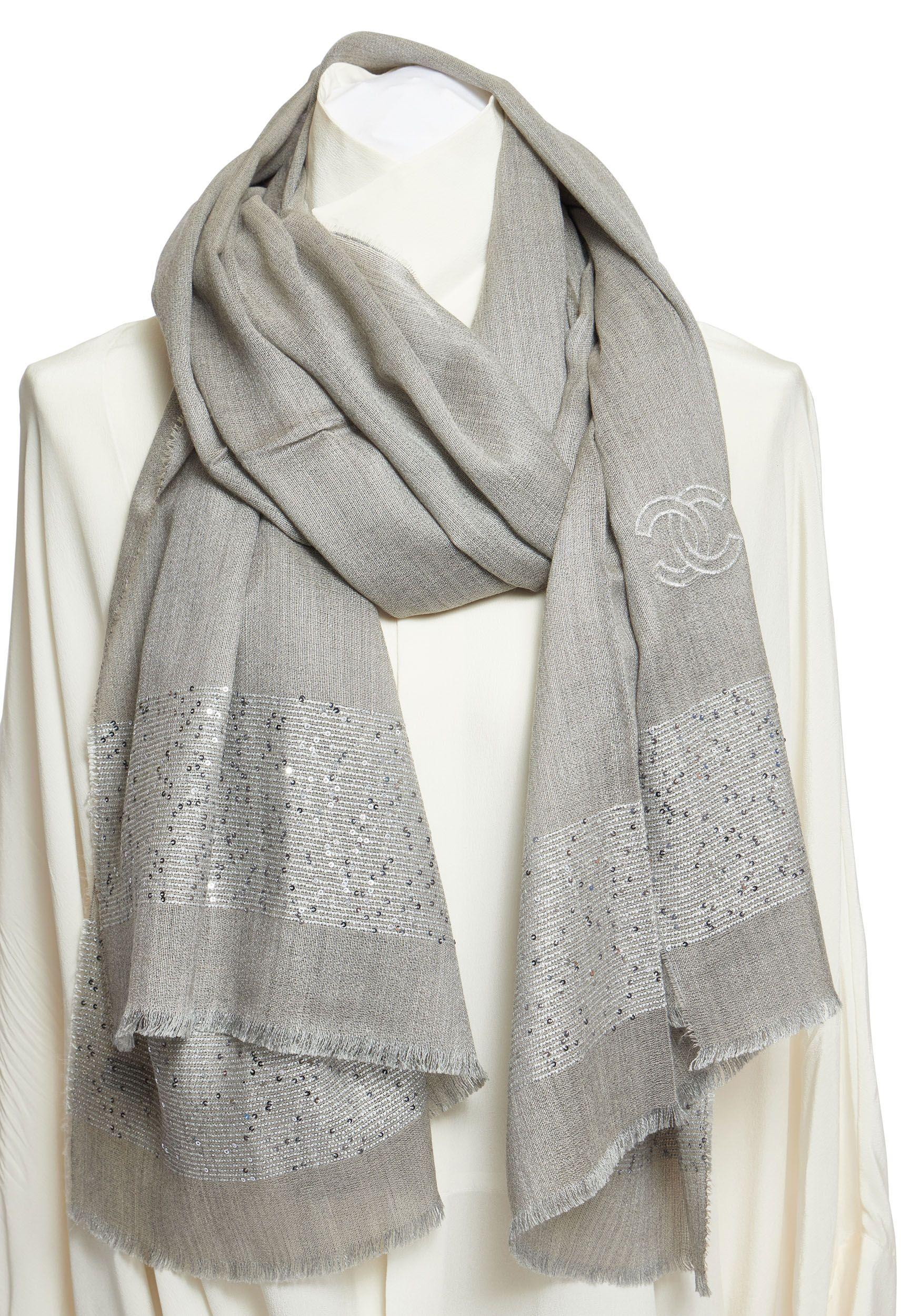 This Chanel cashmere and silk shawl in grey is a must have. The piece shows different grey tones which makes it easy to combine with different outfits. There is a big CC logo webbed in and small sequins are attached to the trim. The scarf is made