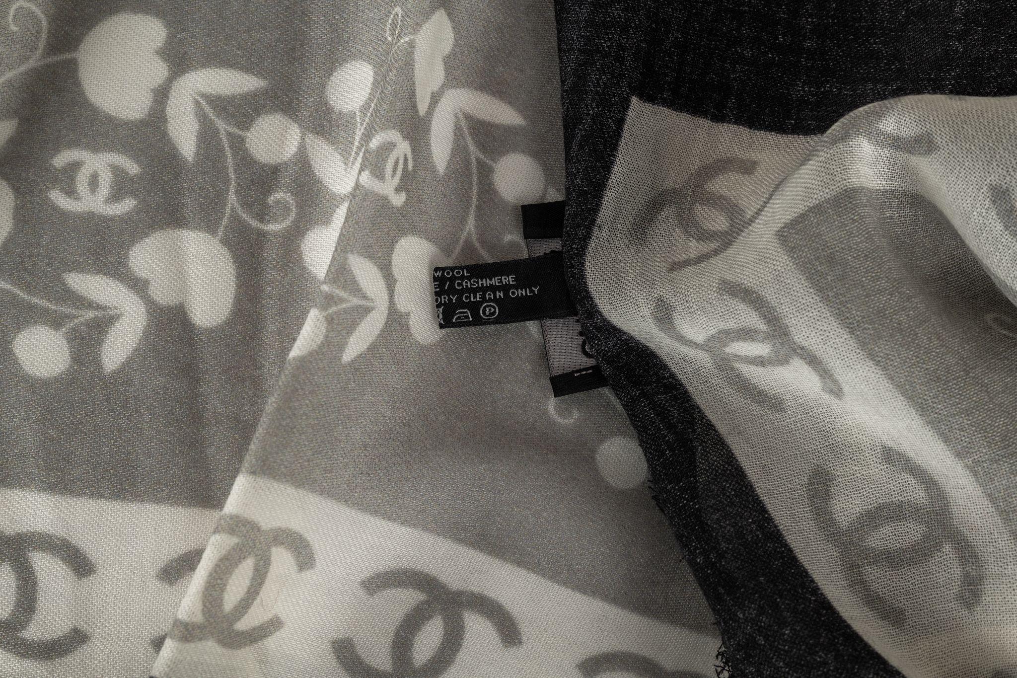 Chanel cashmere shawl in white, grey, black with a big CC logo print in the center. The frame consists of a pattern of hearts and cc logos. The item is in new condition.