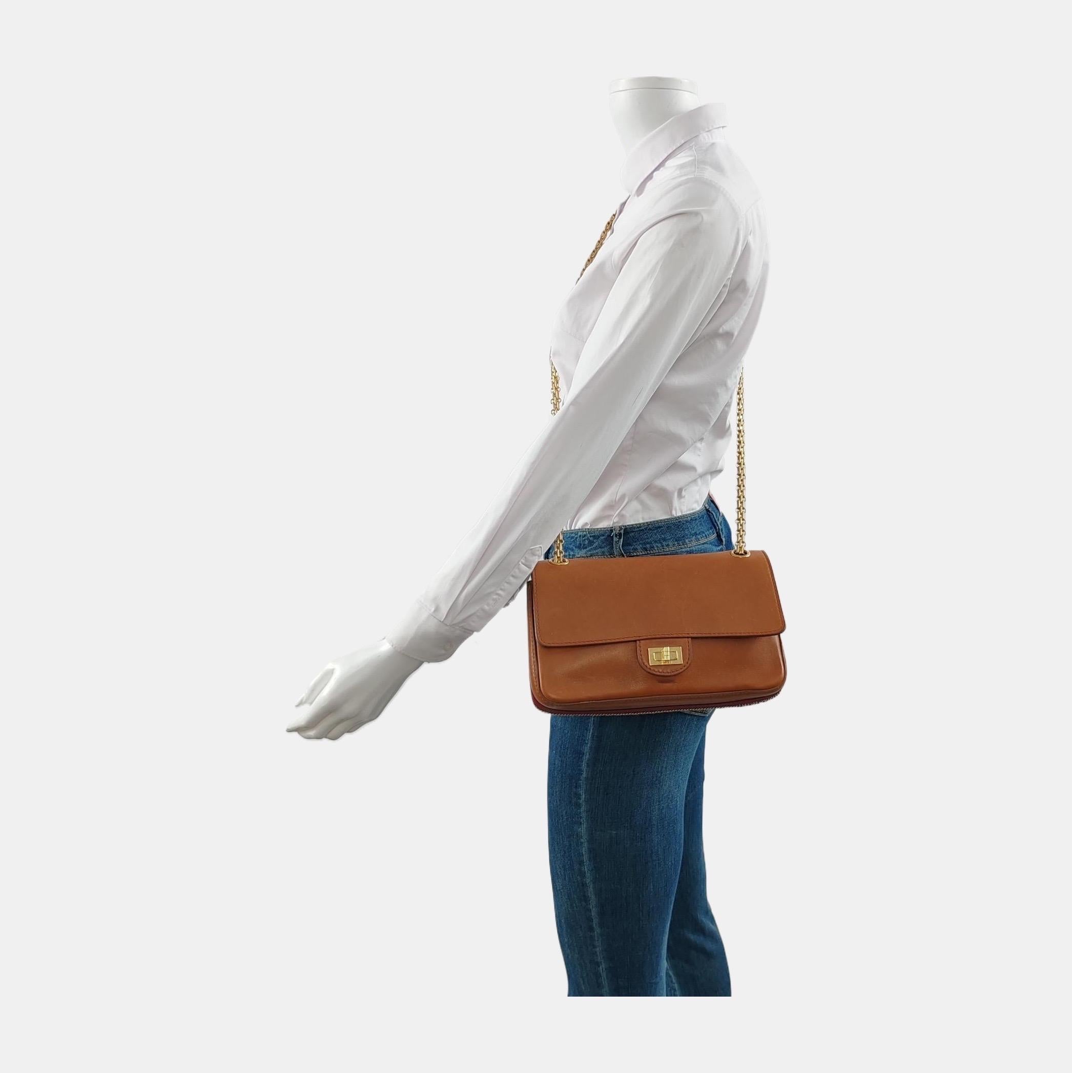 Cette réédition distinguée du modèle Chanel 2.55 se compose d'un luxueux cuir de veau lisse dans une élégante teinte brun cognac, délaissant le traditionnel matelassage à losanges. La quincaillerie et la chaîne en or opulent créent un contraste