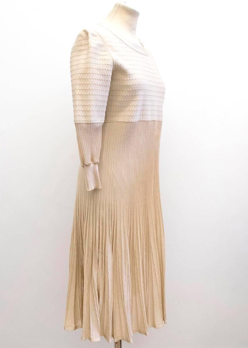 Chanel nude long sleeved, pleated dress.

There are three cream buttons on the left shoulder, which feature the chanel emblem.
The dress is mid length.

Please note, these items are pre-owned and may show signs of being stored even when unworn and