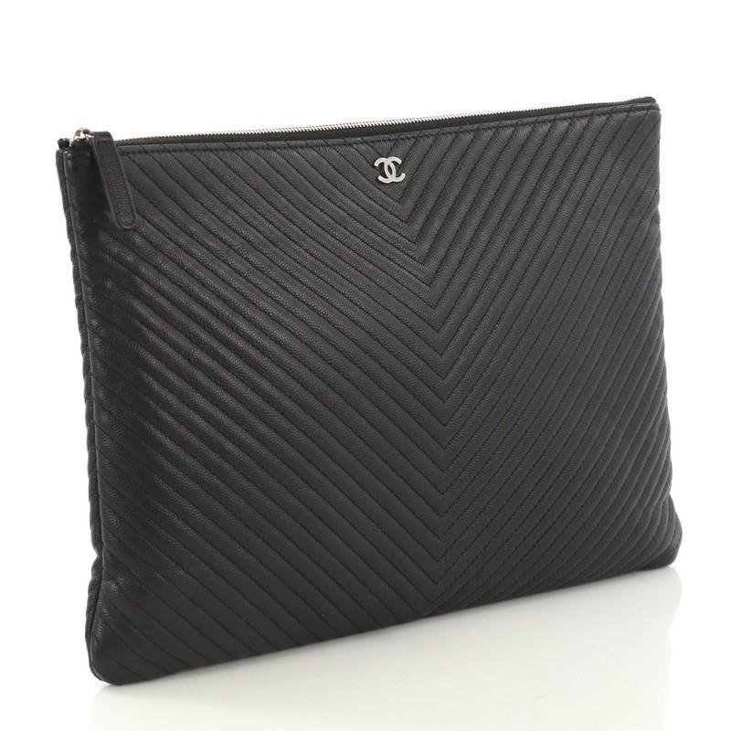 This Chanel O Case Clutch Chevron Caviar Large, crafted from black chevron caviar, features a tiny CC logo on the front and silver-tone hardware. Its zip closure opens to a black nylon interior. Hologram sticker reads: 22181158. 

Estimated Retail