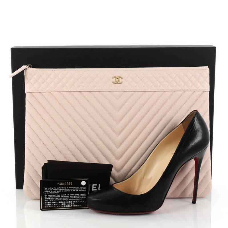 This authentic Chanel O Case Clutch Chevron Caviar Large from 2017 adds a touch of elegance to your everyday outfits. Crafted from light pink chevron quilted caviar leather, this chic clutch features a tiny CC logo on the front and gold-tone