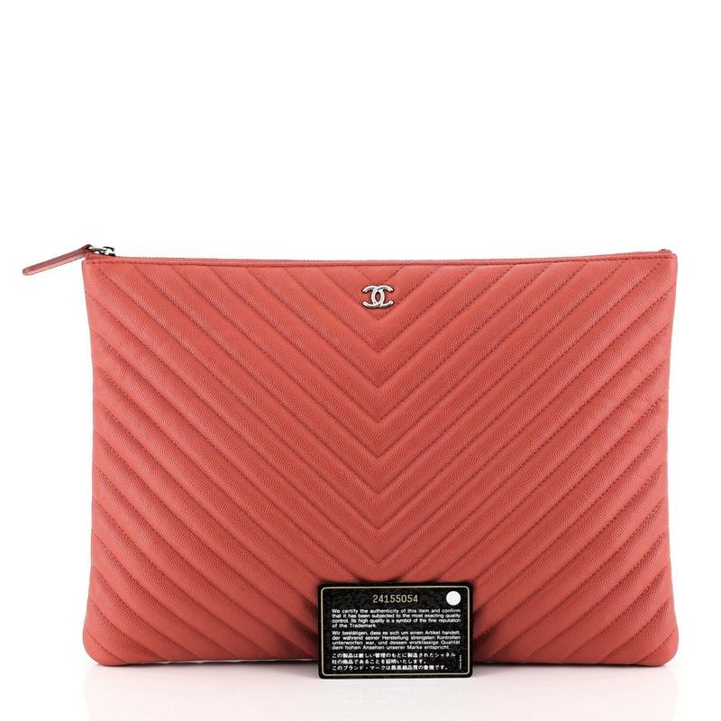 This Chanel O Case Clutch Chevron Caviar Large, crafted from red chevron caviar leather, features a tiny CC logo on the front and silver-tone hardware. Its zip closure opens to a red fabric interior with zip pocket. Hologram sticker reads: 24155054.