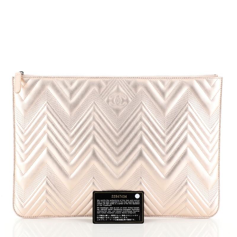 This Chanel O Case Clutch Metallic Chevron Calfskin Large, crafted from pink metallic chevron quilted leather, features CC stitched logo on the front, and silver-tone hardware. Its zip closure opens to a pink fabric interior. Hologram sticker reads: