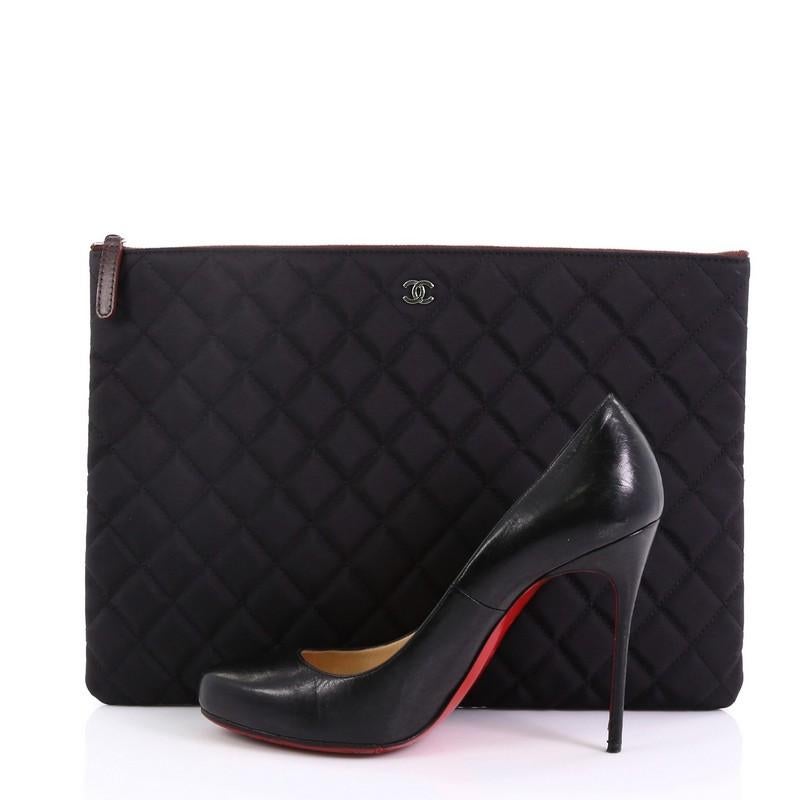 This Chanel O Case Clutch Quilted Nylon Large, crafted from black quilted nylon, features a tiny CC logo on the front and silver-tone hardware. Its zip closure opens to a burgundy quilted nylon interior. Hologram sticker reads: 18727143. **Note: