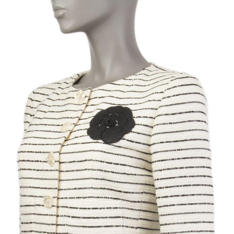 Chanel collarless blazer in off-white cotton-blend and black sequin stripes (probably as content tag is missing) with black camelia on the chest. Two front pockets. Opens with square checked mother-of-pearl buttons. Lined in silk (probably as