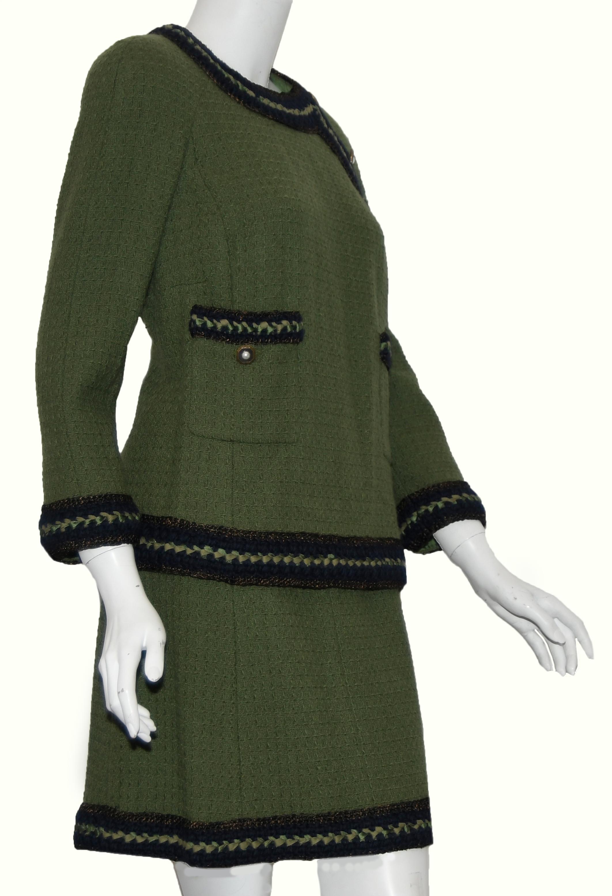 Chanel olive green skirt suit includes navy blue trim on sleeves, cuffs and hem of jacket and skirt.  The navy trim is accentuated with green ribbon and gold tone faux pearl buttons.  The skirt has a back zipper for closure and the top, 3 buttons