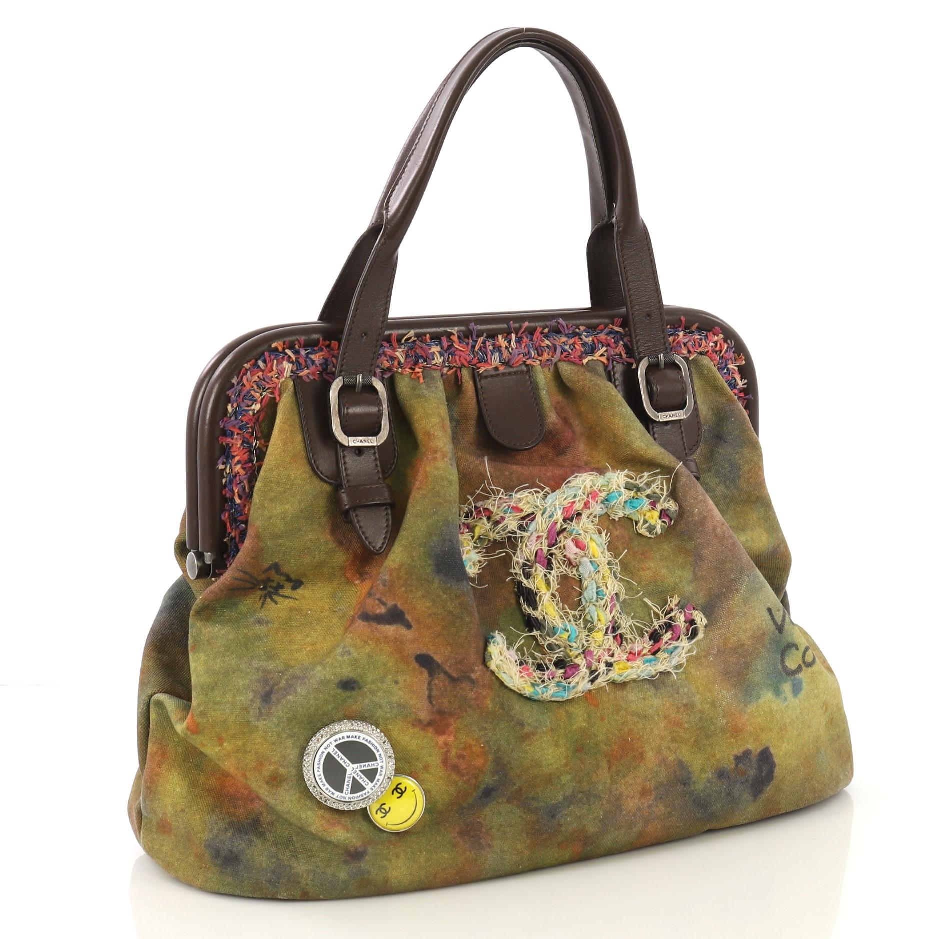 This Chanel On The Pavements Graffiti Bowling Bag Canvas, crafted from khaki washed canvas, features dual leather top handle with buckle details, hand-written graffiti and spray-painted design, CC fabric patch logo in boucle tweed, decorative pins,