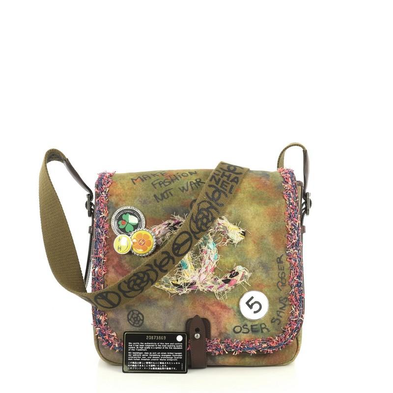 This Chanel On The Pavements Graffiti Messenger Bag Canvas Small, crafted in green canvas with multicolor graffiti print, features decorative pins, graffiti and spray-painted design, crossbody strap, and aged silver-tone hardware. Its snap button