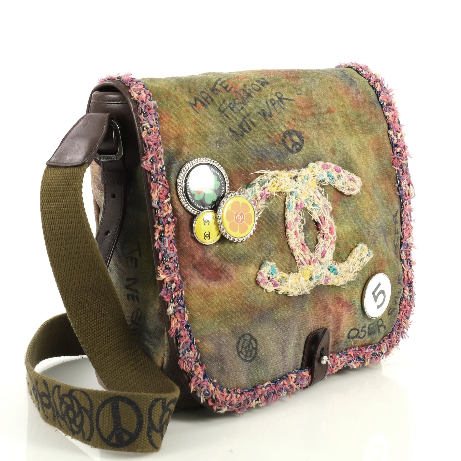 This Chanel On The Pavements Graffiti Messenger Bag Canvas Small, crafted in green printed canvas, features decorative pins, graffiti and spray-painted design, crossbody strap, and ruthenium-tone hardware. Its snap button closure opens to a red