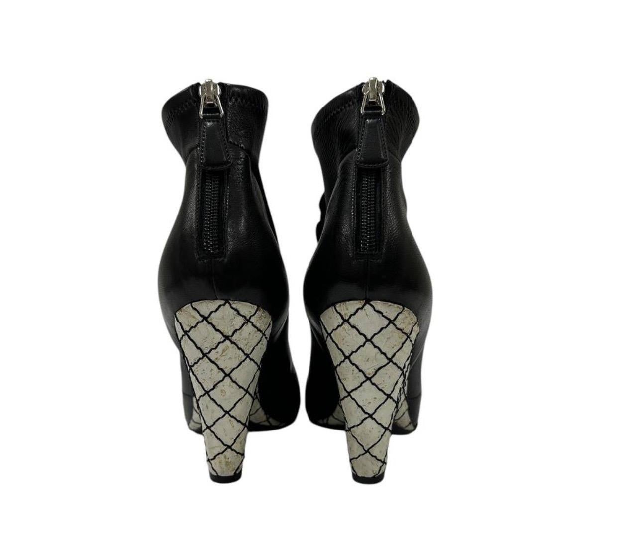 Fabricada en suave piel negra con un diseño peep-toe. Parte delantera detallada con flores de camelia de cuero de gran tamaño. Cierre trasero con cremallera, plantilla acolchada. El escultural tacón de cuña presenta un estampado gráfico en