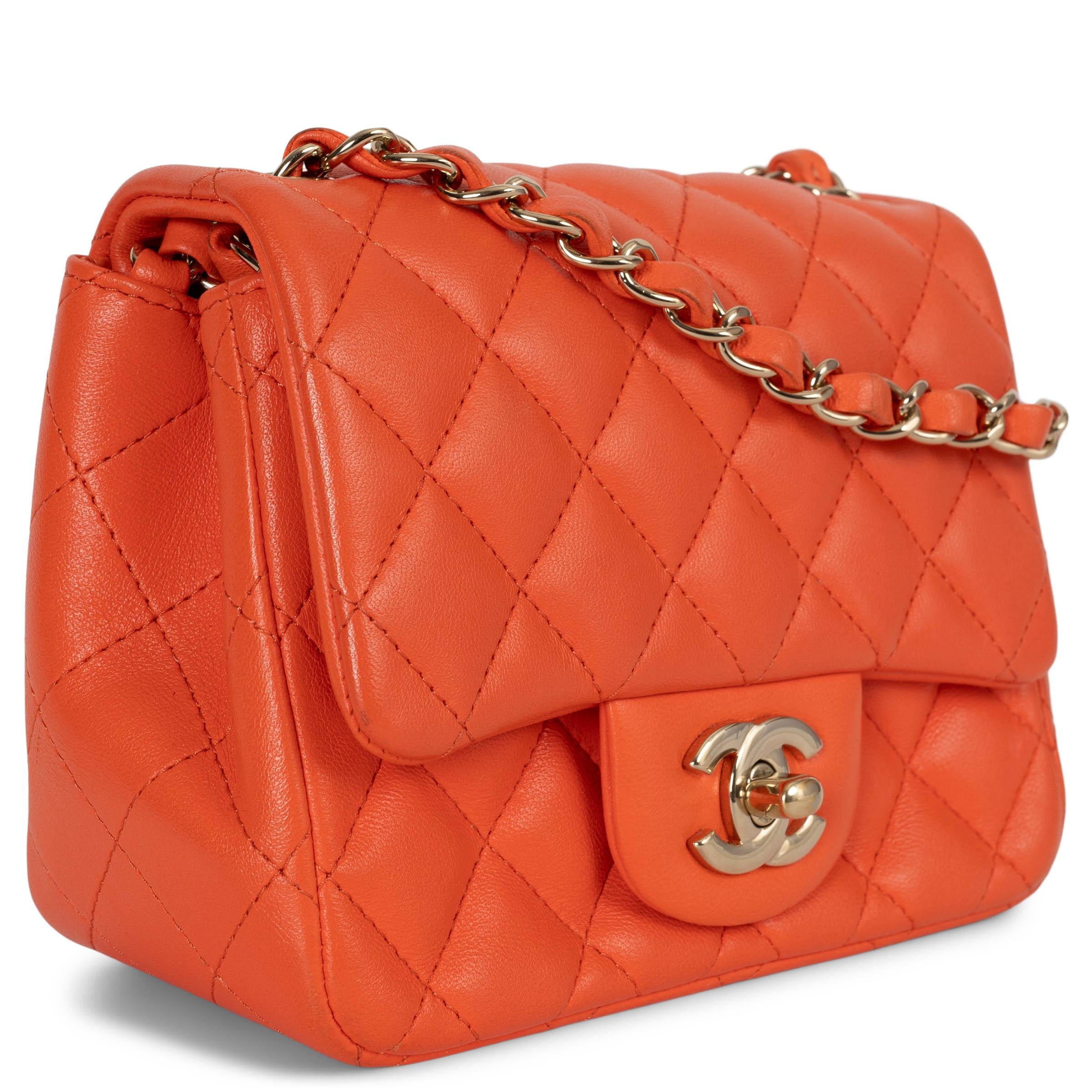 This 100% authentic Chanel Mini Square Flap Shoulder Bag is crafted from vibrant orange quilted lambskin leather and accented with elegant light gold-tone hardware. Featuring a classic open pocket on the outside back, it closes securely with the