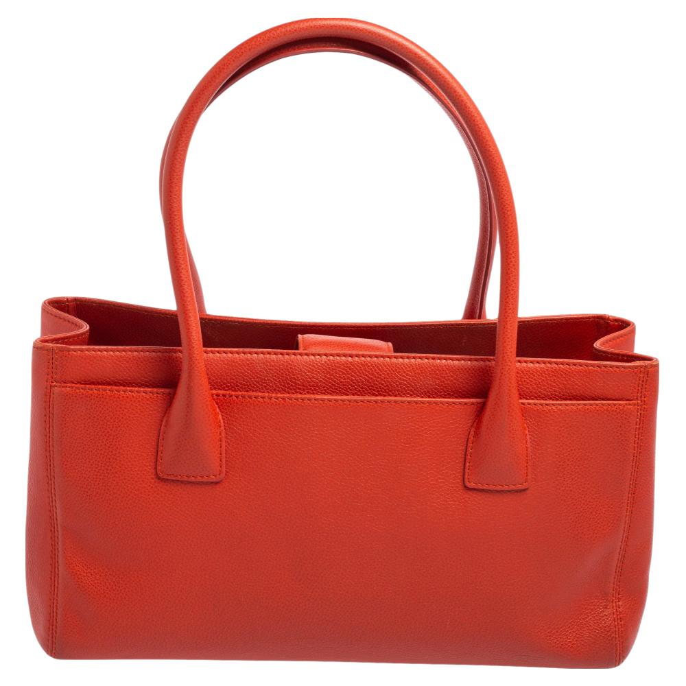 This Cerf tote from Chanel is a perfect blend of function and style. It features an orange leather construction that is enhanced with a metal CC logo on the front and dual top handles. It is equipped with a spacious interior that can easily hold