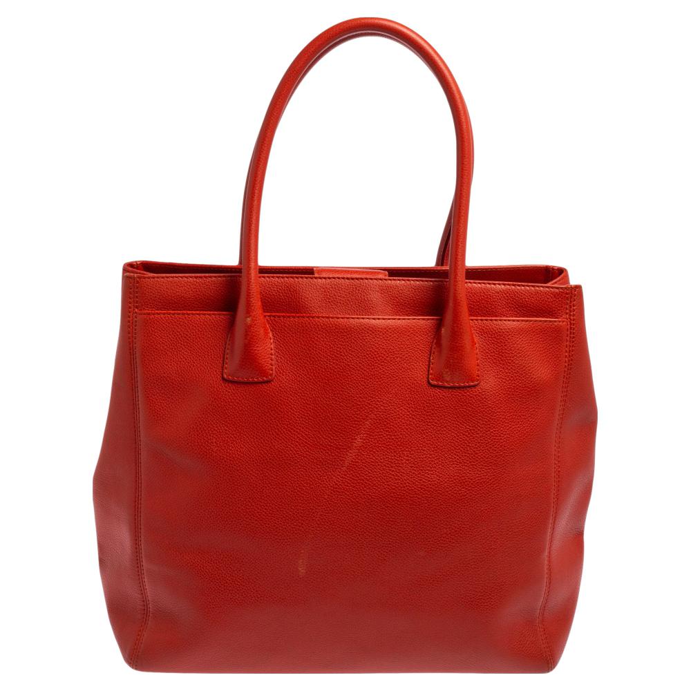 This Cerf tote from Chanel is a perfect blend of function and style. It features an orange leather construction that is enhanced with a metal CC logo on the front and dual top handles. It is equipped with a spacious interior that can easily hold