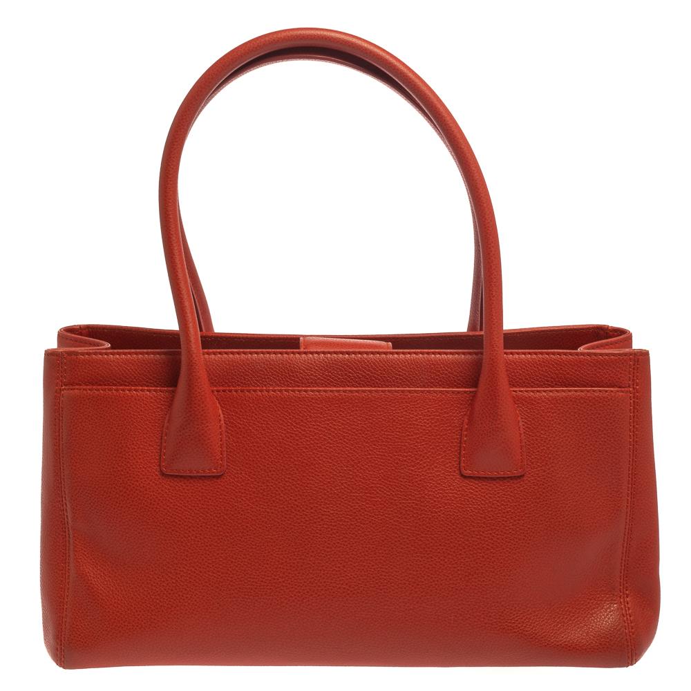 This Cerf Executive tote from Chanel is a perfect blend of functional ease and style. It features an orange leather construction that is enhanced with a silver-tone CC logo on the front and dual top handles. It is equipped with a spacious