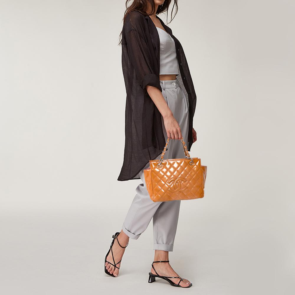 A timeless creation from the house of Chanel, this shopper tote is petite and pretty. Featuring the signature quilt and the 'CC' logo on the patent leather exterior, this orange bag is held by two handles. Equipped with metal studs on the base and a