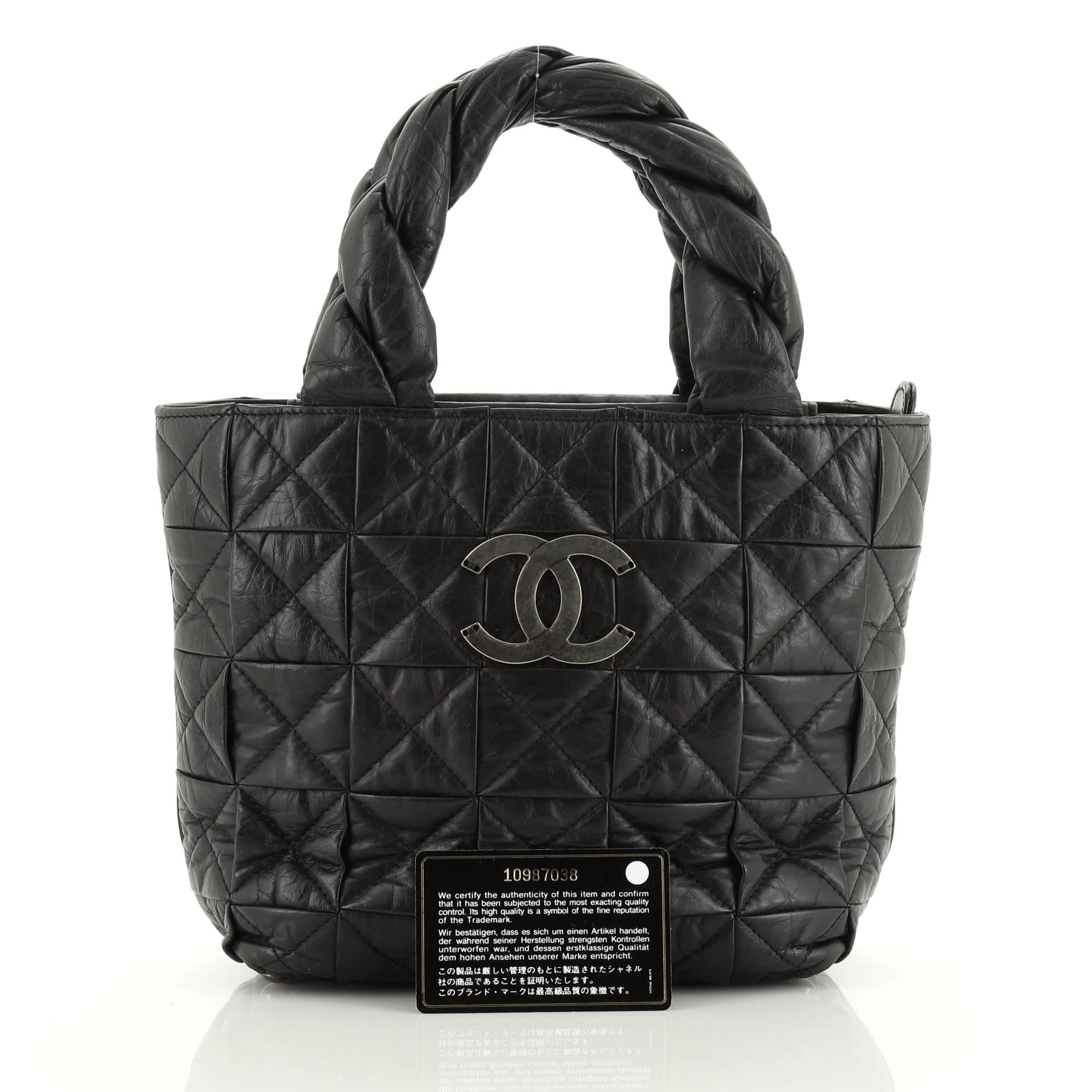 This Chanel Origami Tote Quilted Aged Calfskin Small, crafted from black quilted aged calfskin leather, features dual top twisted calfskin leather handles, frontal silver Chanel CC logo, and silver-tone hardware. Its zip closure opens to a black
