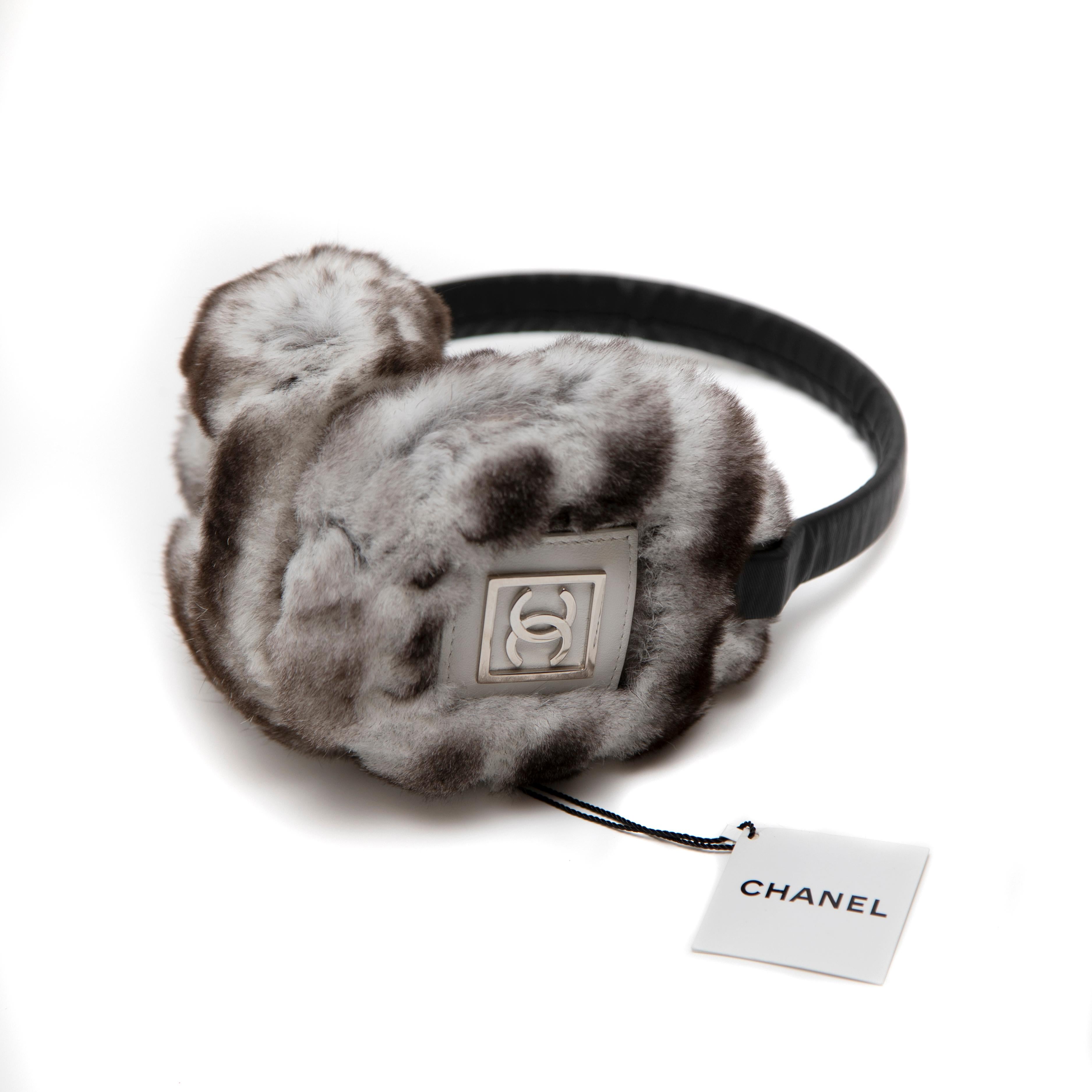 Indulge in luxurious winter warmth with these brand-new Chanel Orylag (Rabbit) Fur Earmuffs. Crafted from ultra-soft fur, these earmuffs feature a sleek design with silver-tone metal CC logos mounted on white leather patches for a refined touch of