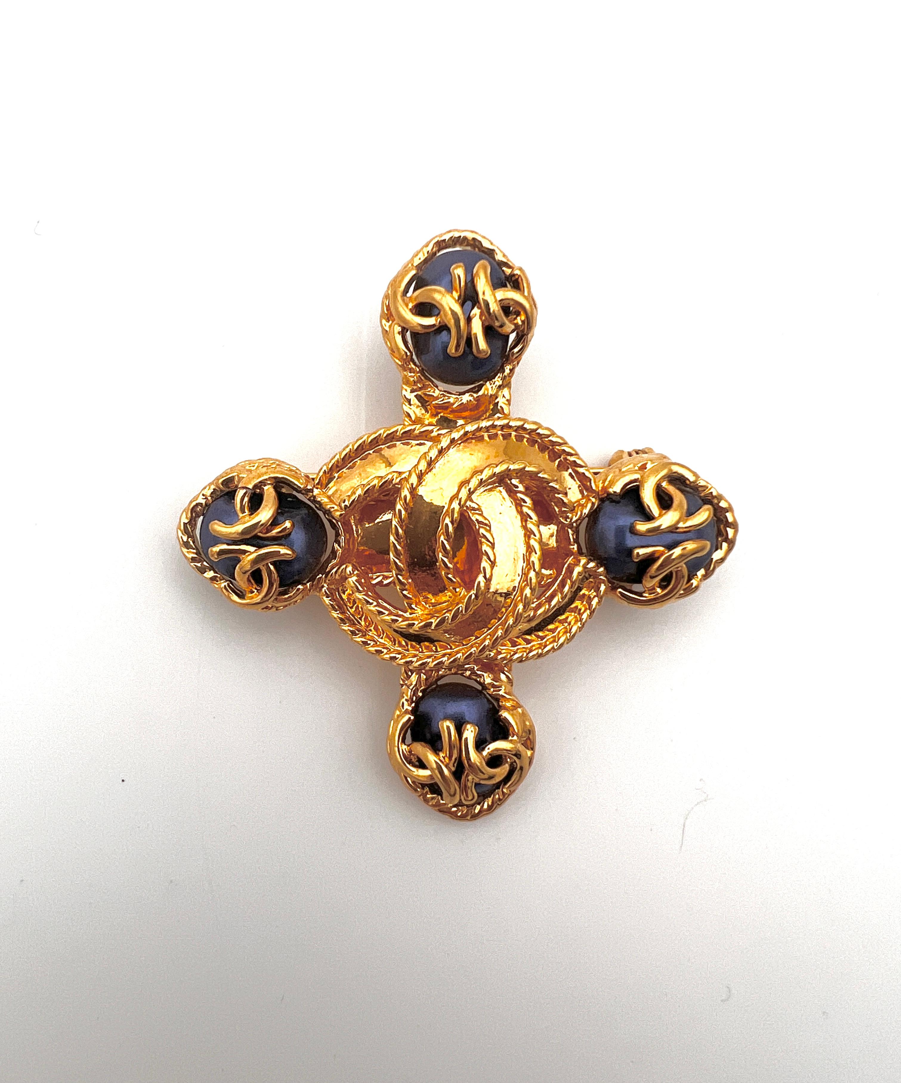 Superbe broche Chanel en forme de croix de Malte avec le logo CC de Chanel au centre. Sur chaque extrémité de la croix se trouve un cabochon bleu/gris avec 2 logos Chanel sur chacun d'eux.
Une belle broche datant de 1995, avec un timbre au